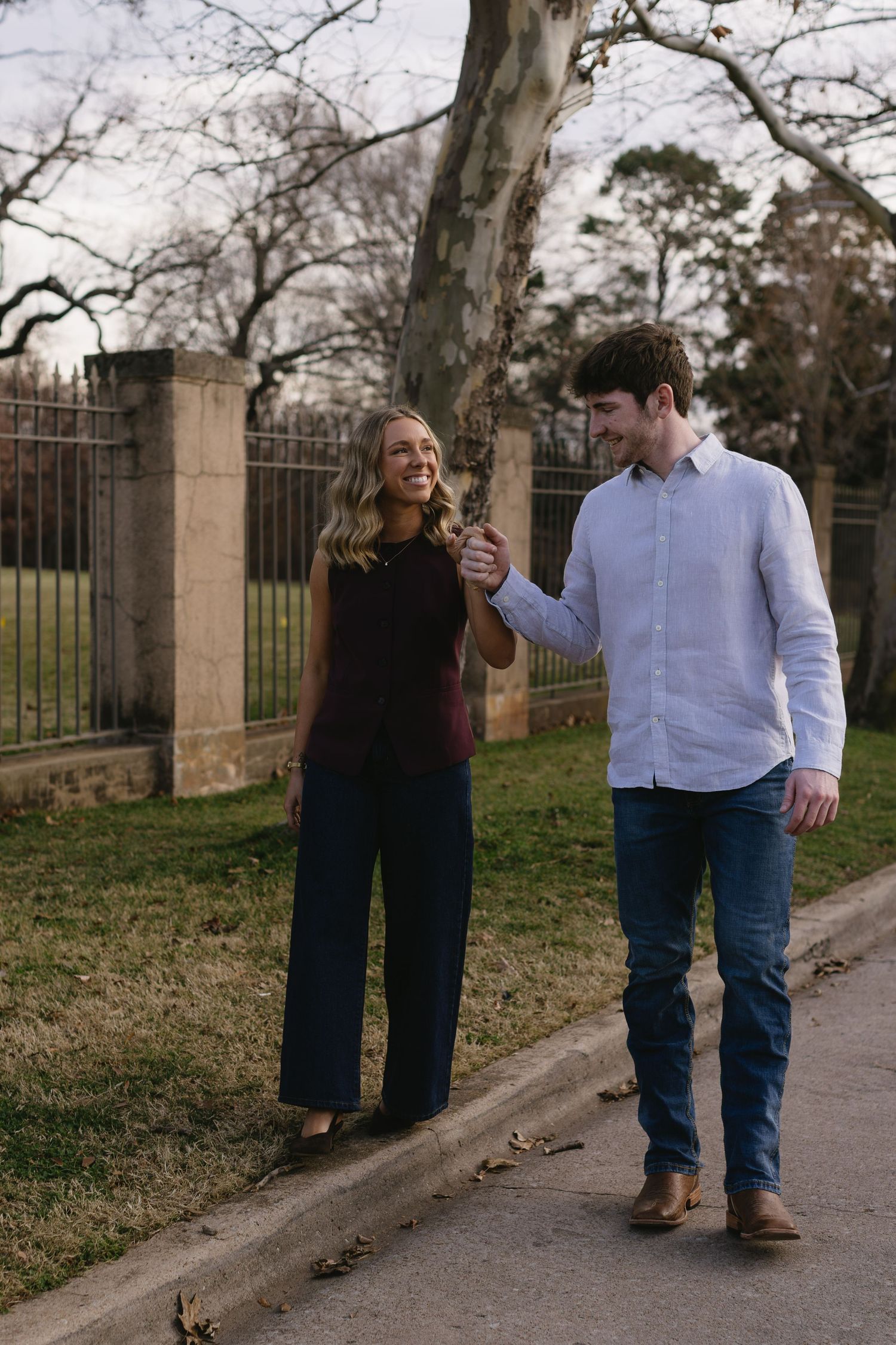 Couple walking and laughing together on a stone path near an iron fence.