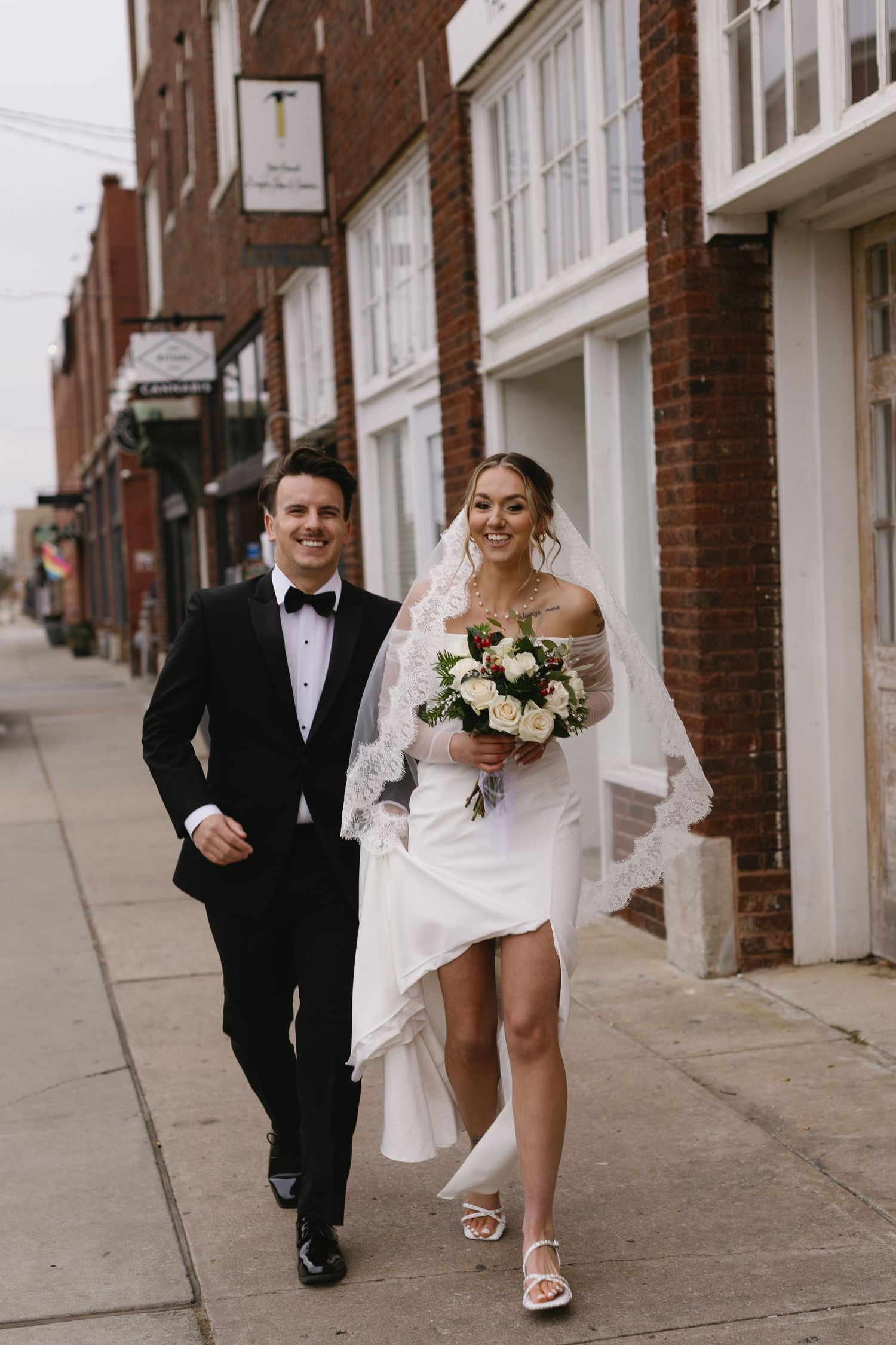 A joyful couple walks down a city sidewalk after their wedding ceremony.