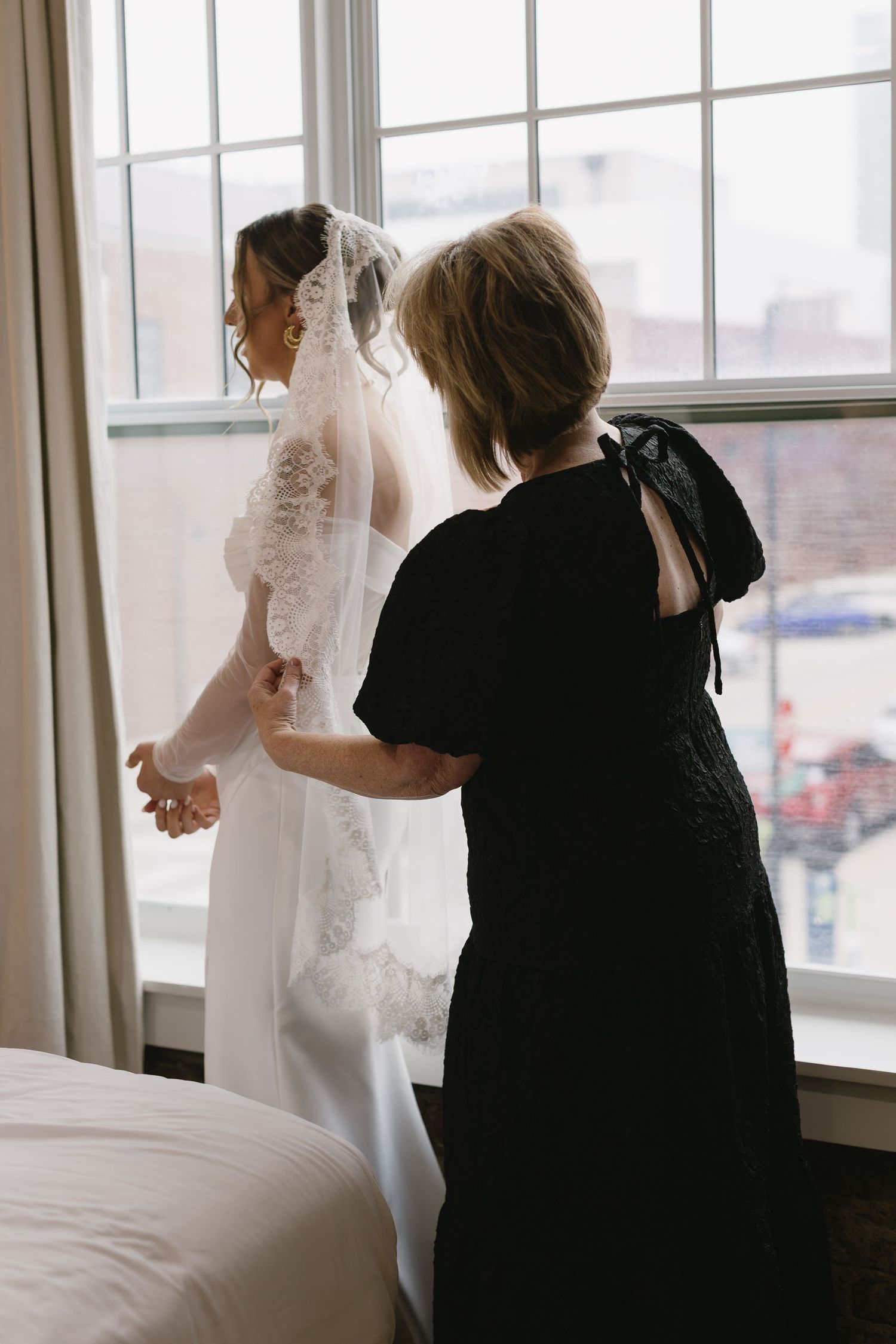 Wedding dress fitting session with attendants by large windows in natural light.