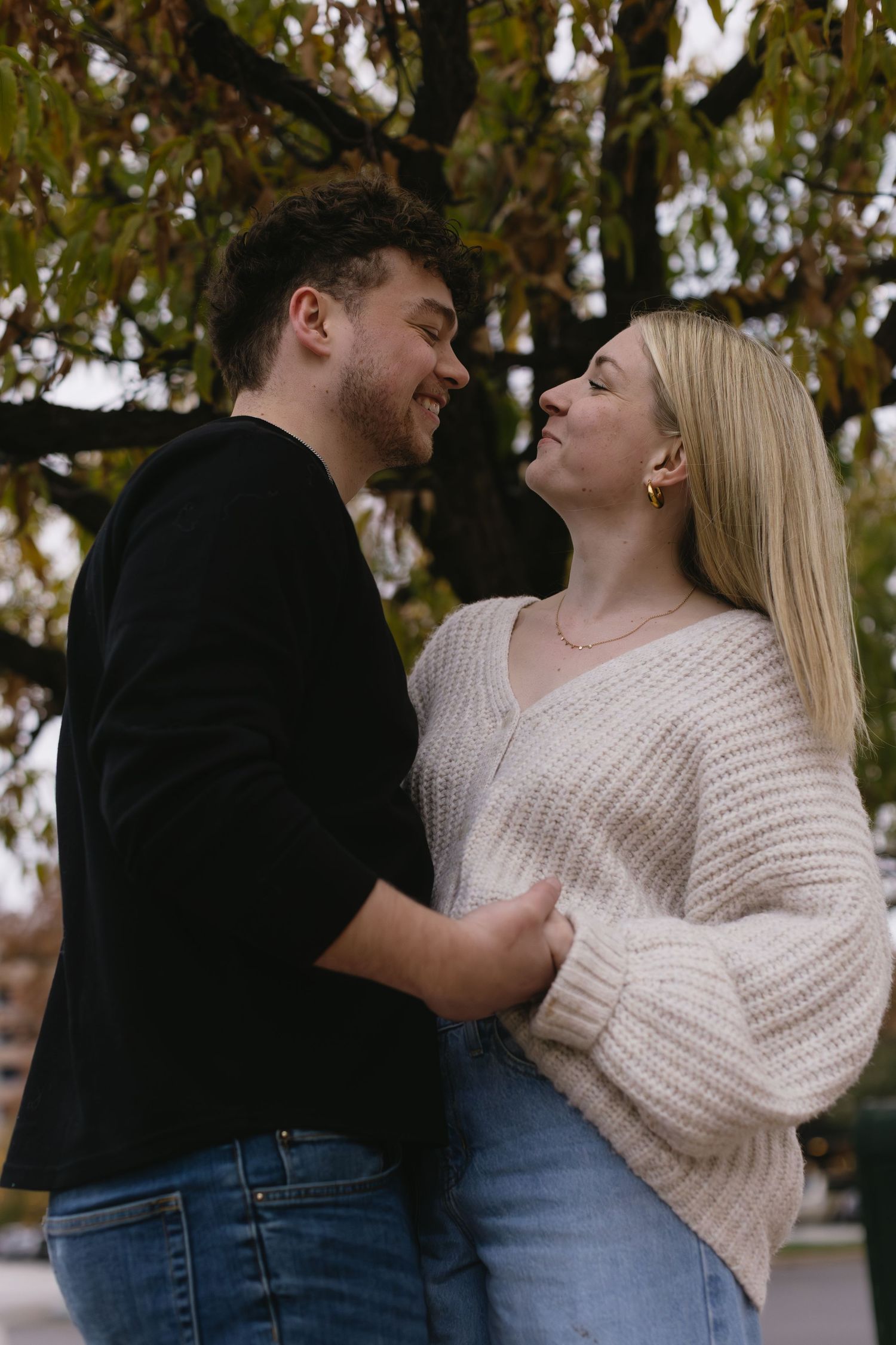 An intimate autumn portrait of a couple in casual attire sharing a tender moment under fall foliage.