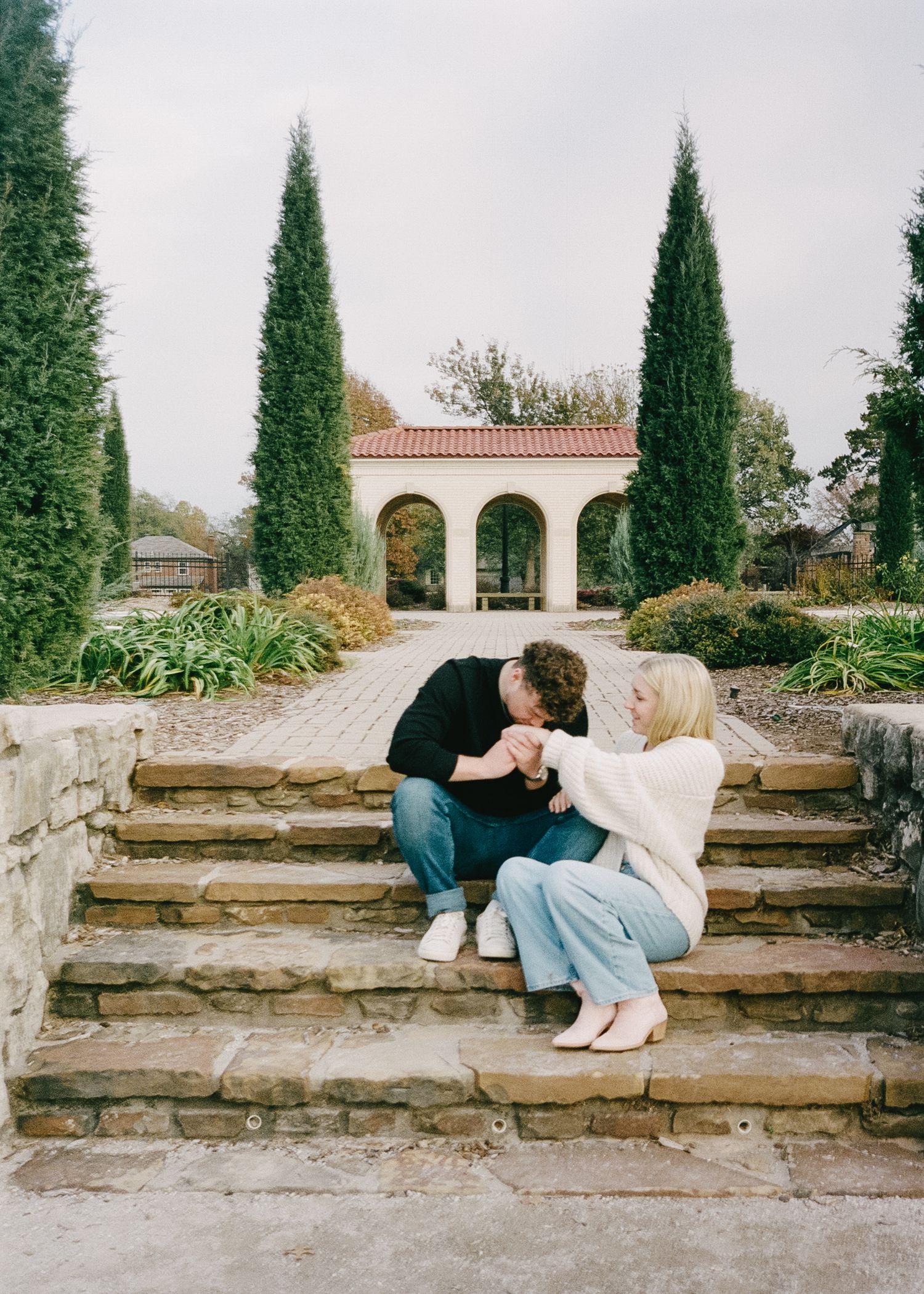 Couple sitting on stone steps with cypress trees in background.