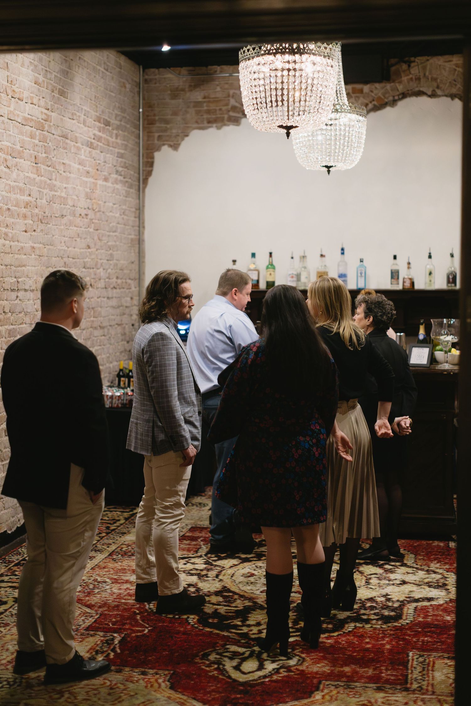 Wedding guests mingling in an exposed brick venue space with ornate chandeliers.
