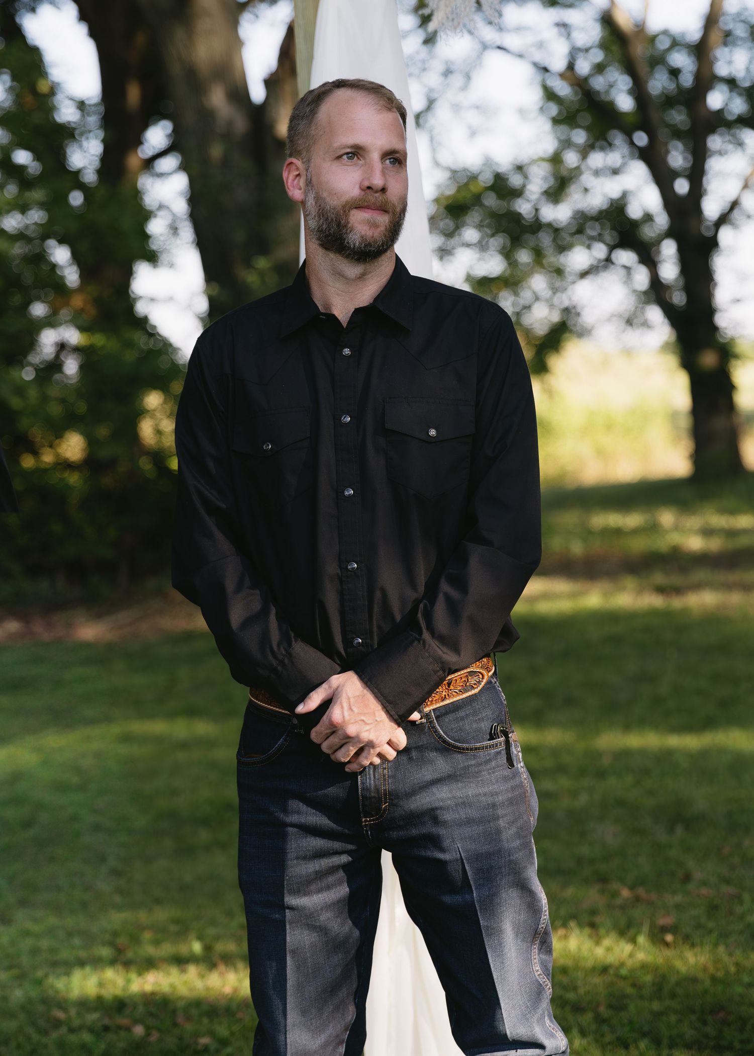 Man in black shirt and jeans stands casually outdoors.