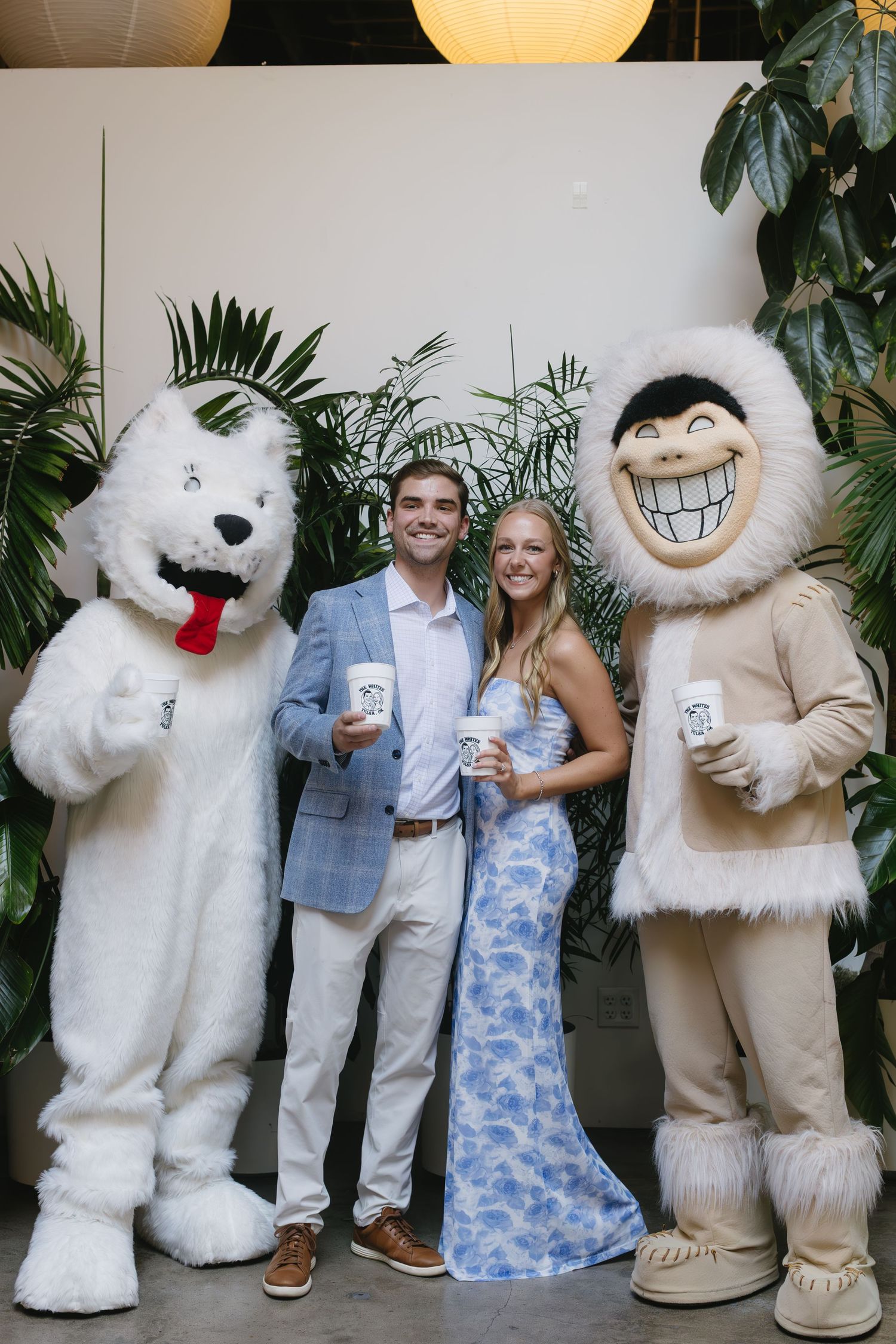 Couple posing for photos with large polar bear mascots at an event celebration.