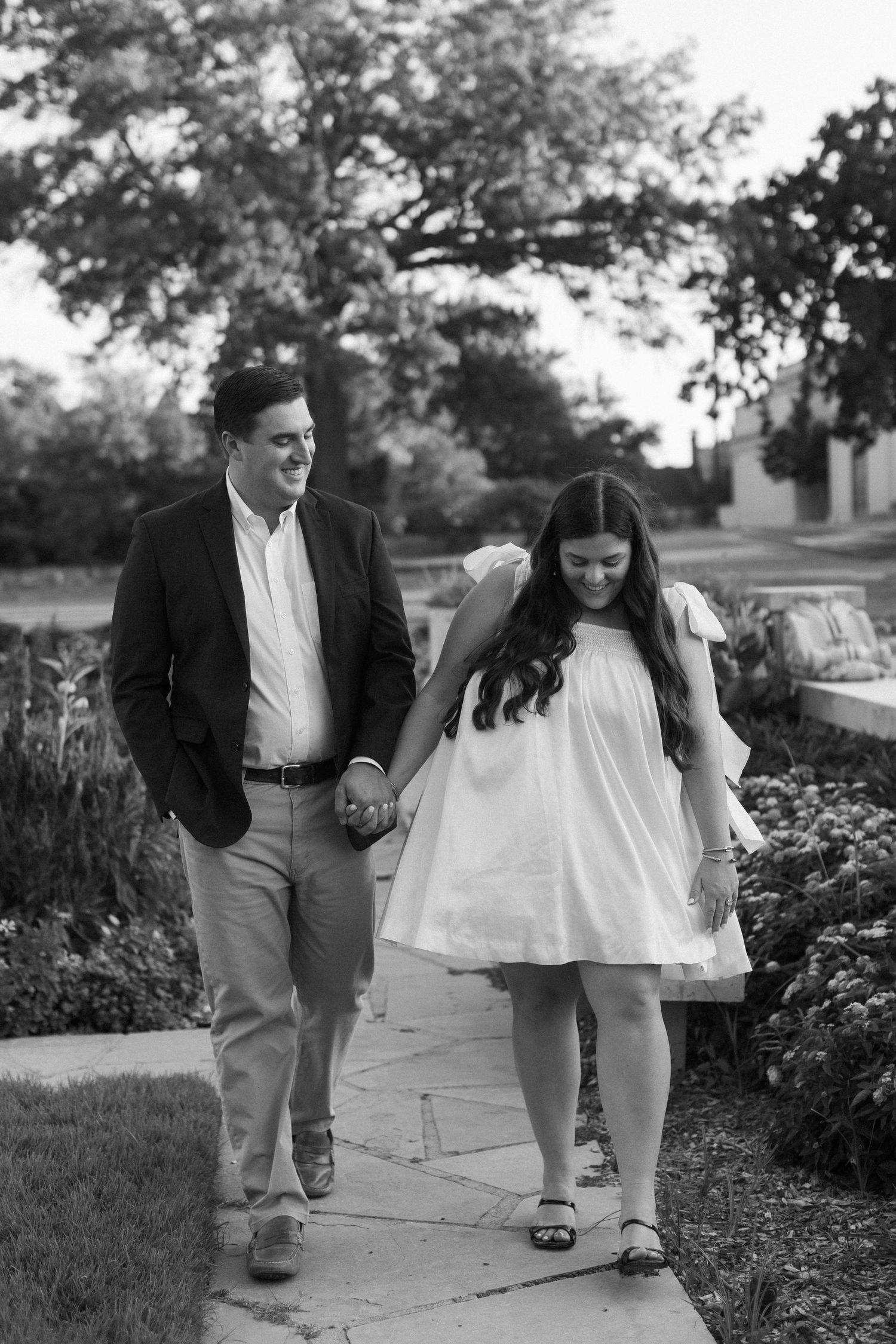 Black and white engagement photos show couple walking together on garden pathway.
