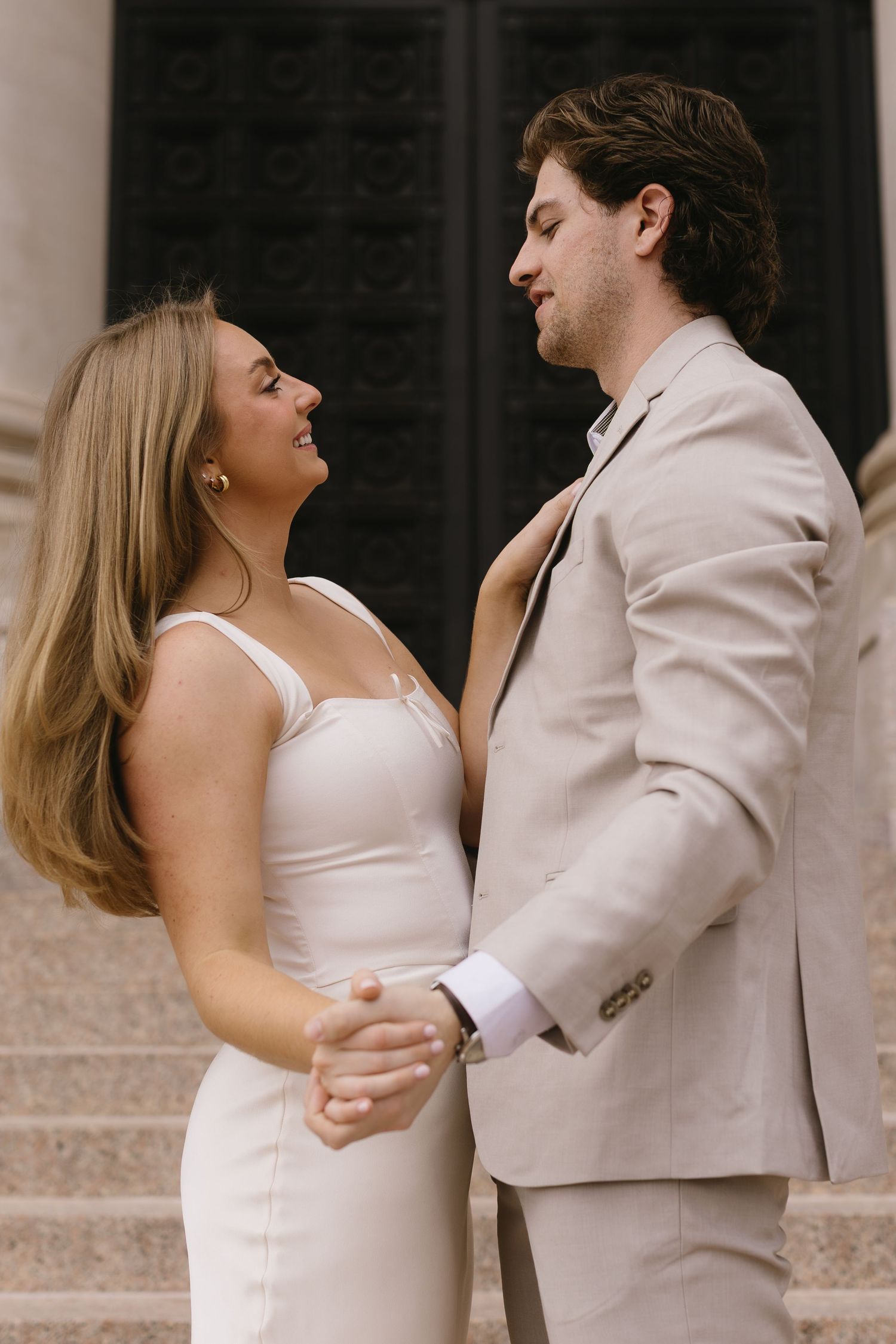 A romantic couple in matching beige and white formal wear share an intimate moment on stone steps.