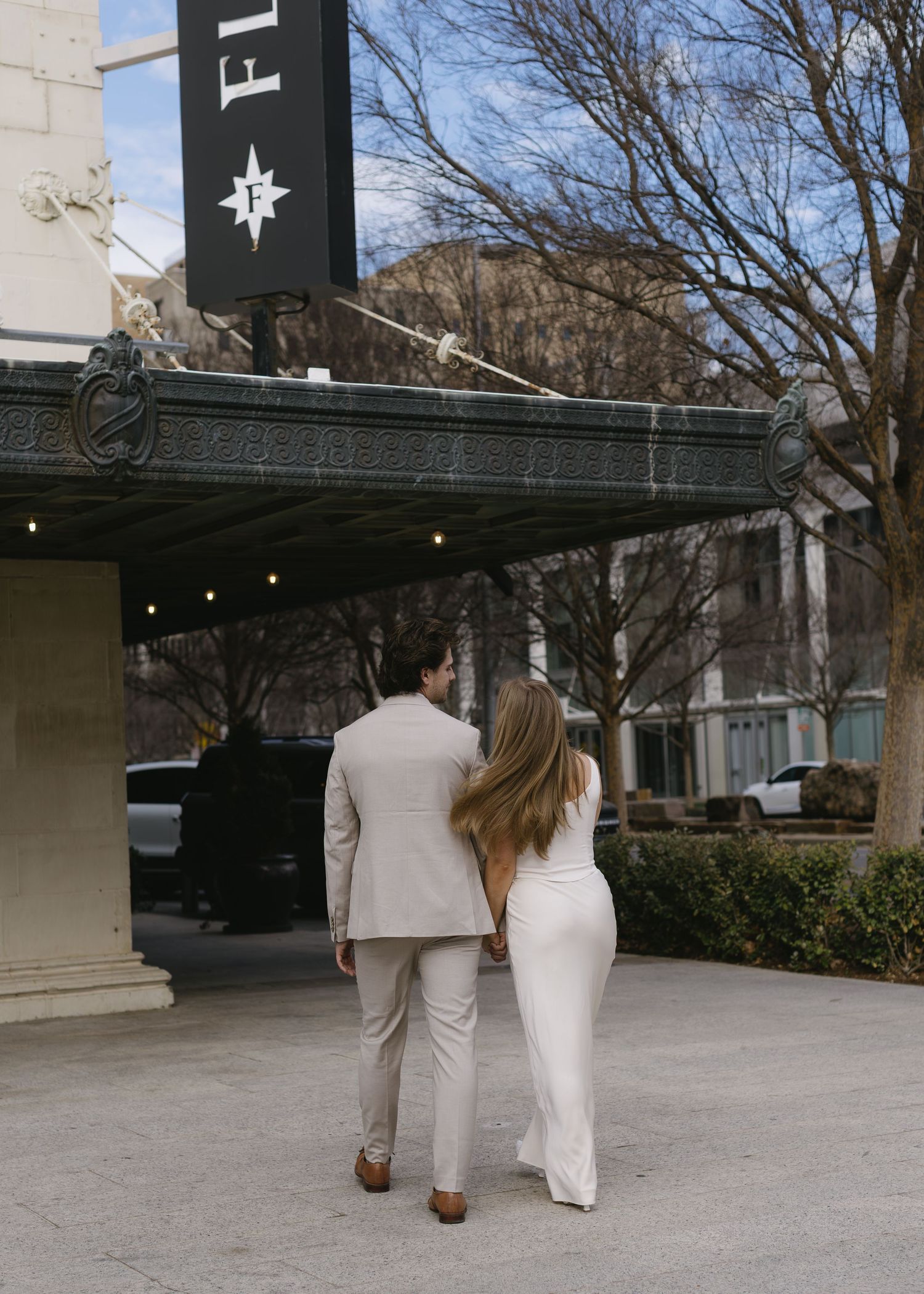 A couple in light colored formal wear walking away together on a winter day.