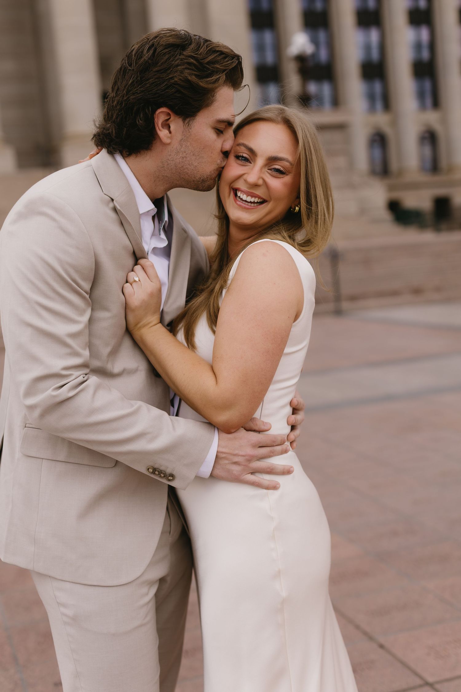 A joyful couple in neutral tones shares laughter and embraces on stone steps.