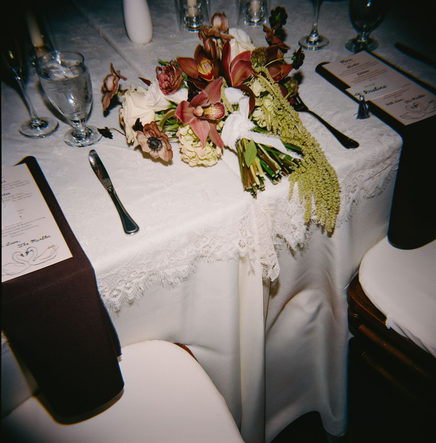 Elegant wedding reception table settings with white linens and floral centerpieces in a dimly lit venue.