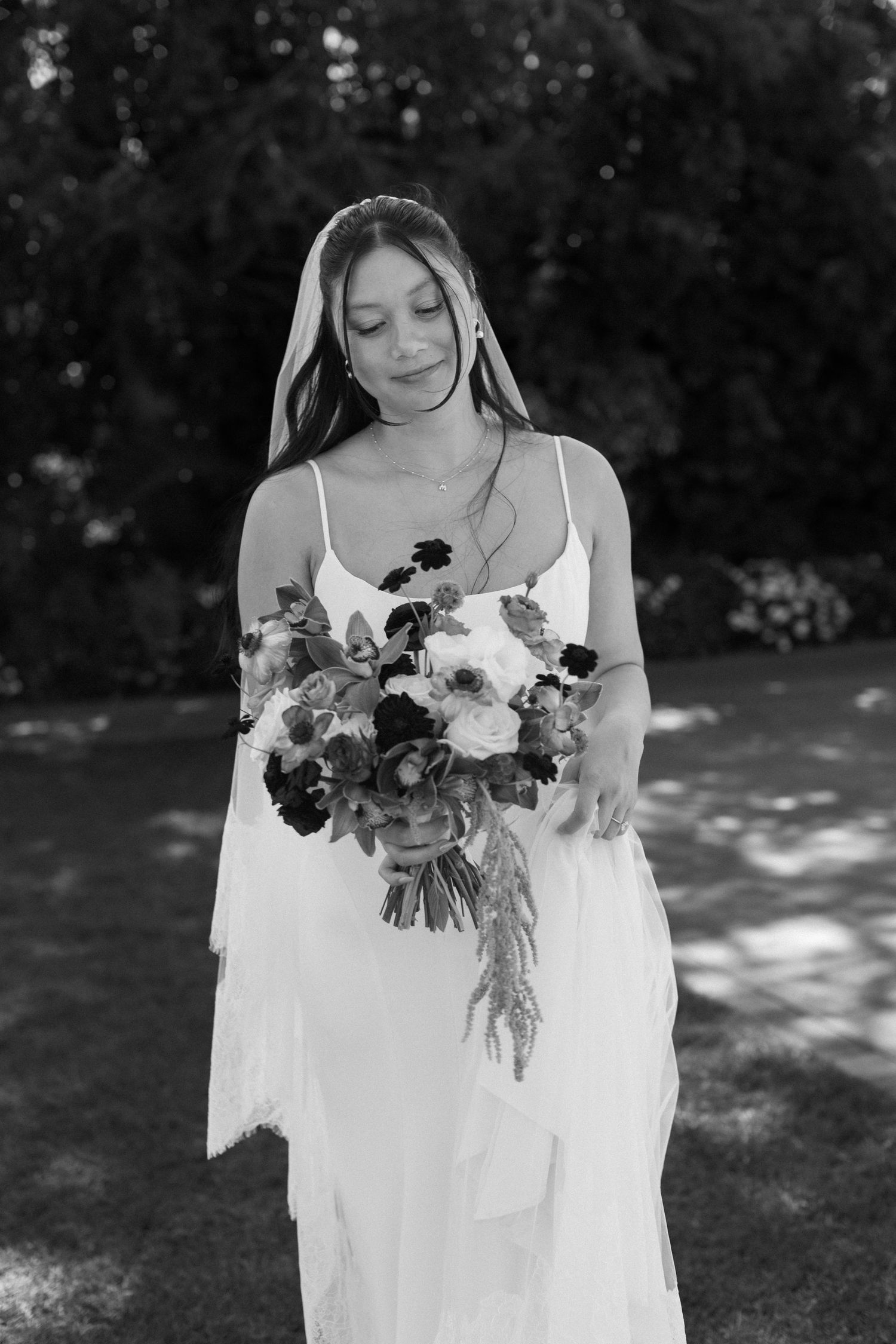 A bride in white holds a romantic bouquet of flowers in a garden setting.