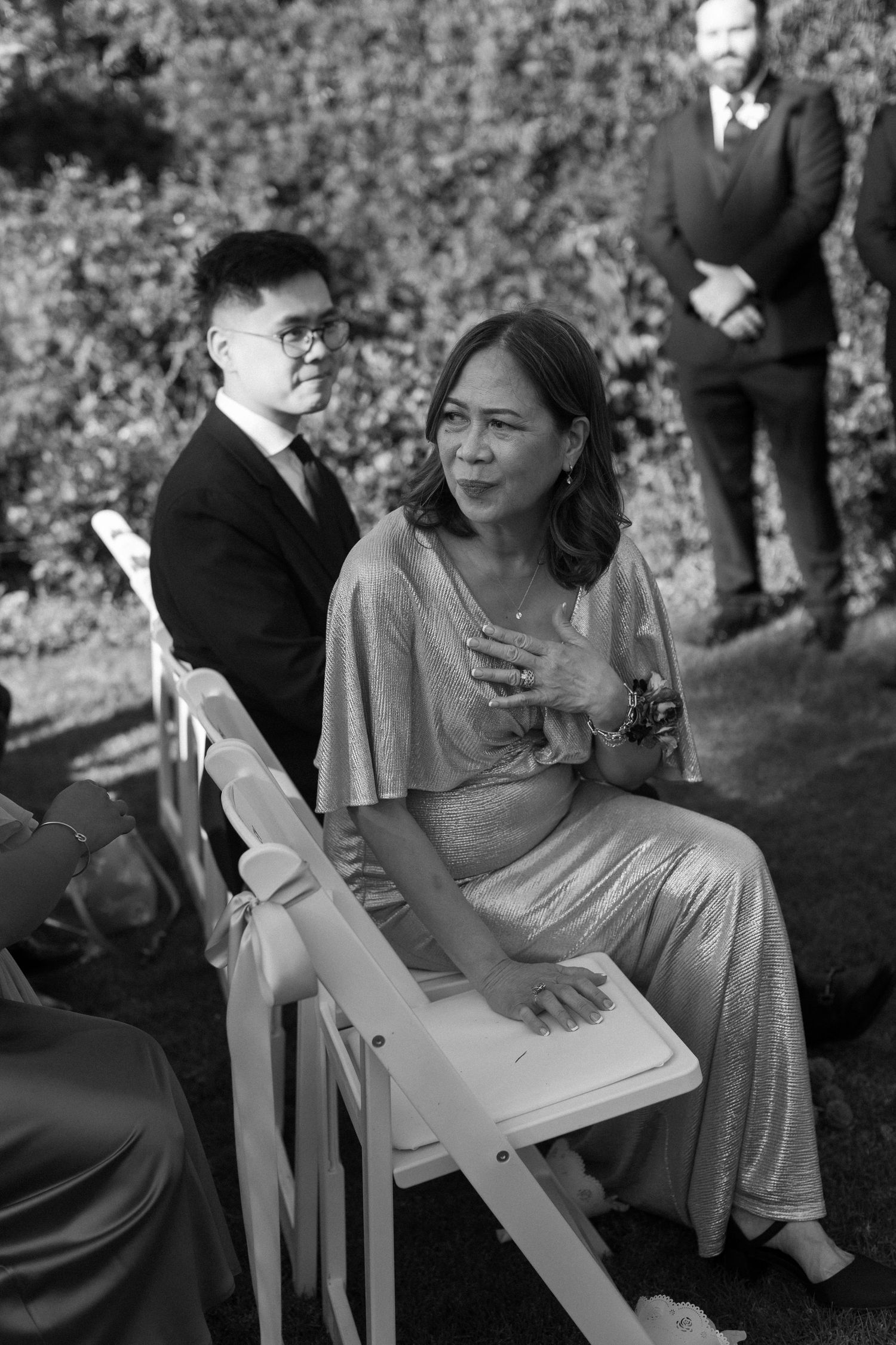 Wedding guests in formal attire seated outdoors during ceremony.