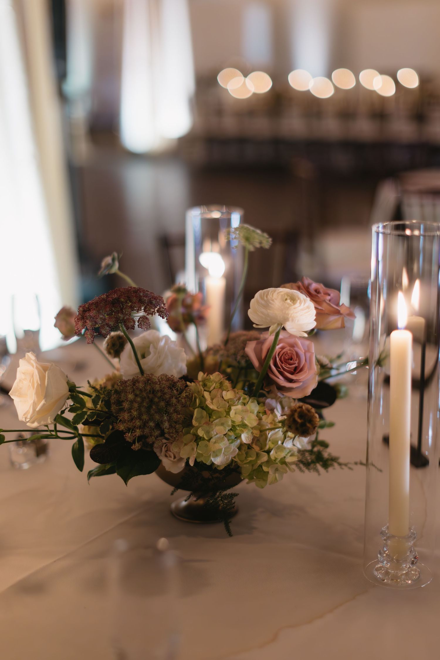 Elegant wedding reception table decorated with pink roses, candles and glassware.