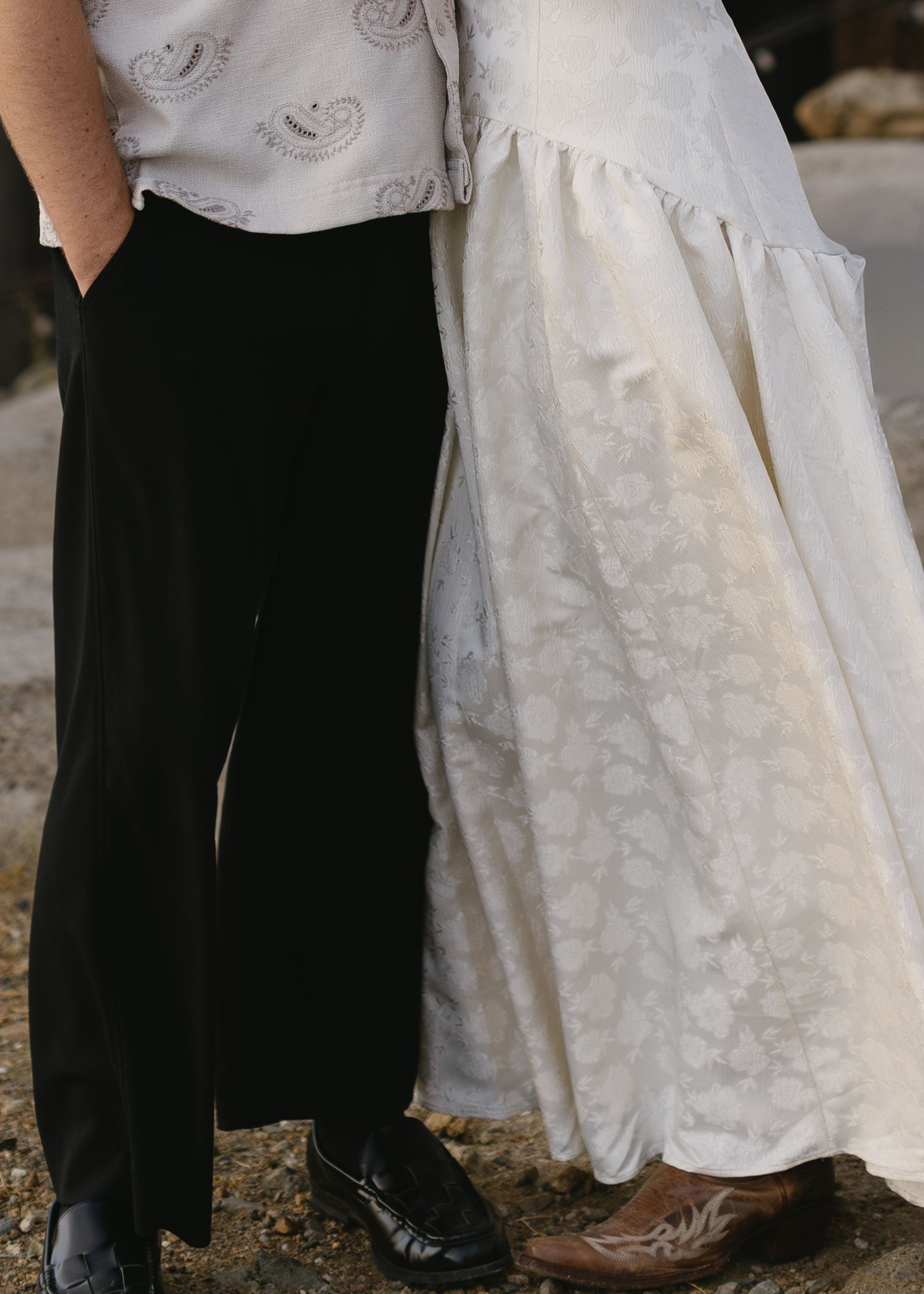 Close-up view of formal attire showing black dress pants next to a flowing white paisley patterned dress with dress shoes.