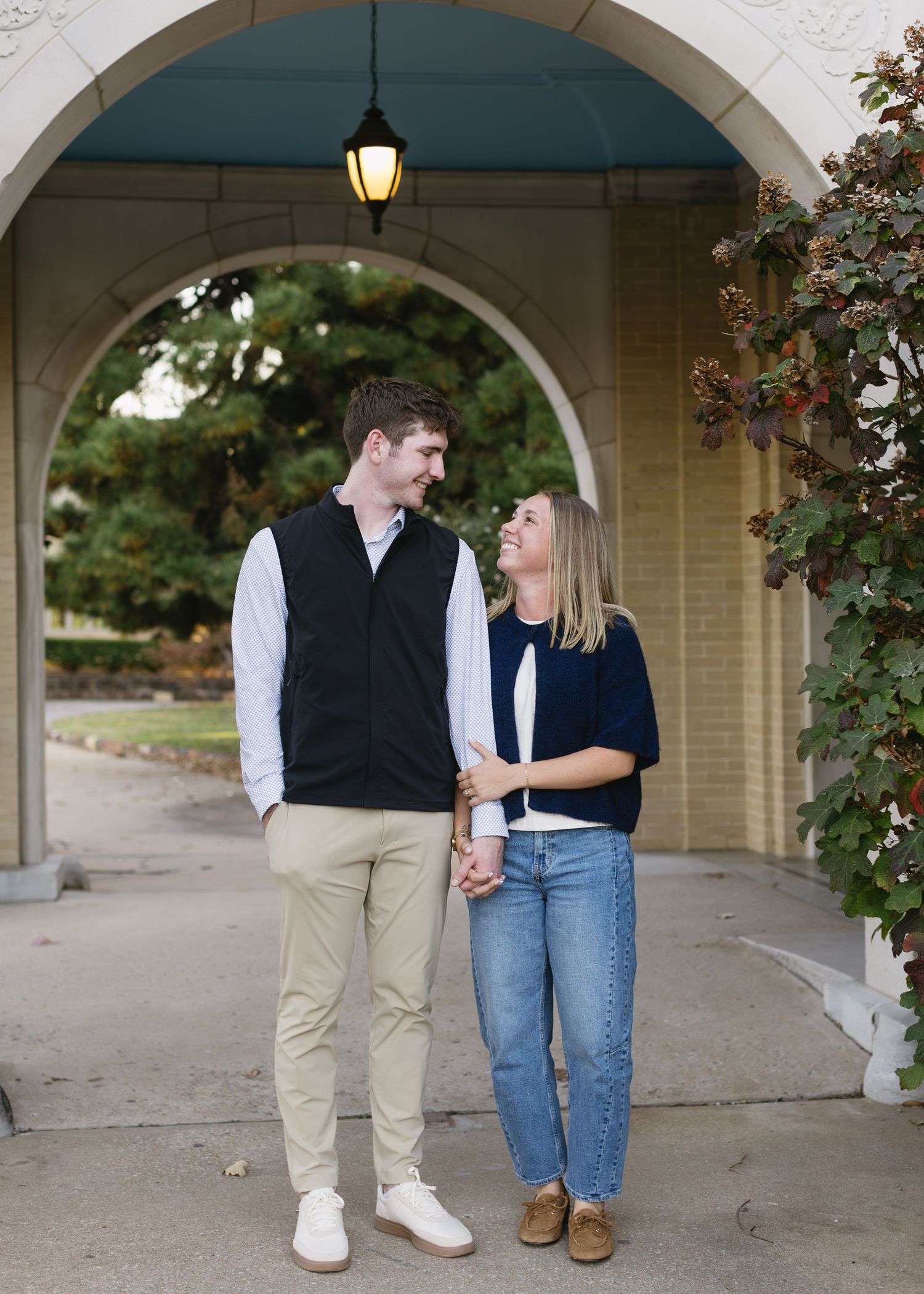 A couple standing under an arched walkway in casual matching outfits.