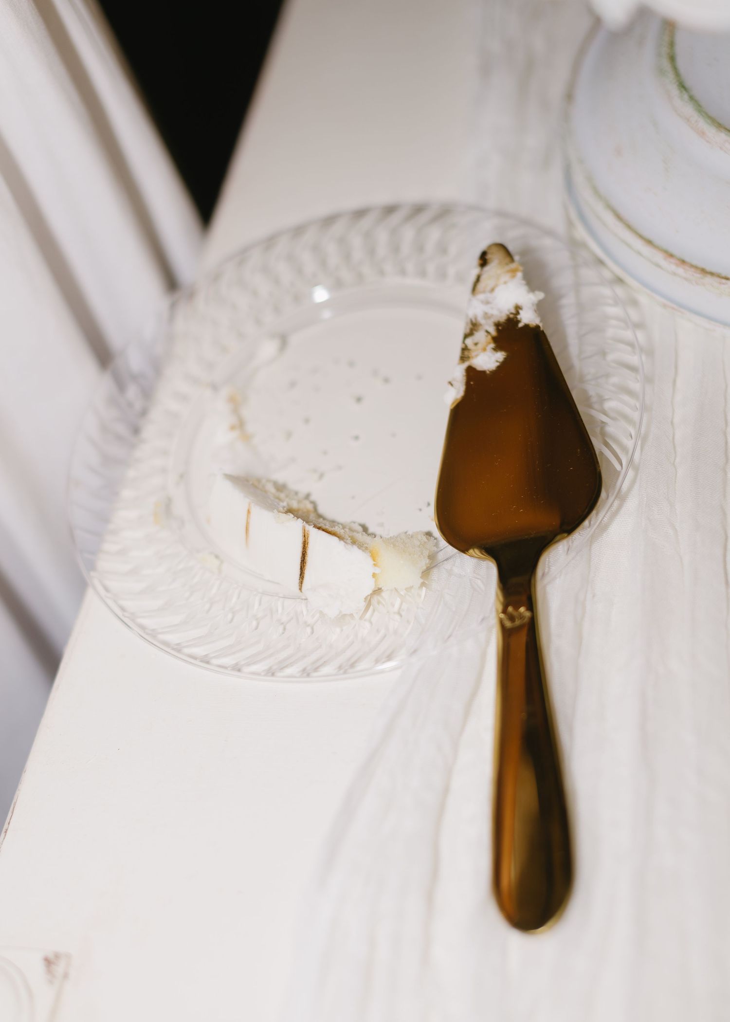 Used cake plate with gold serving utensil on white tablecloth.