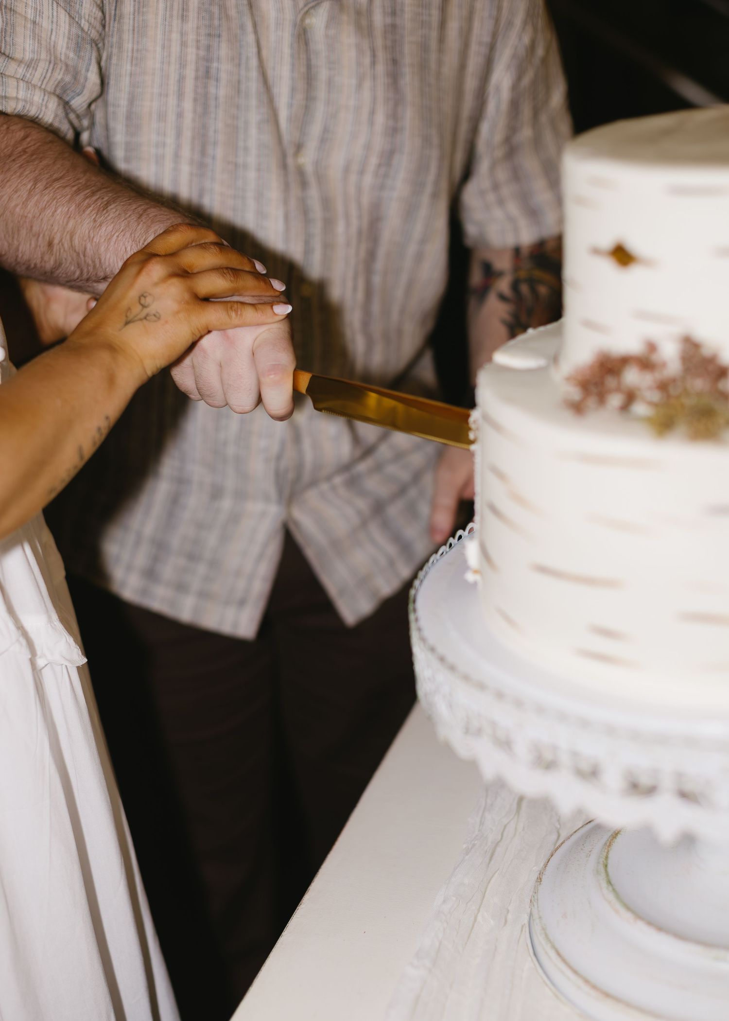 Close-up of hands cutting into a white wedding cake with decorative details.