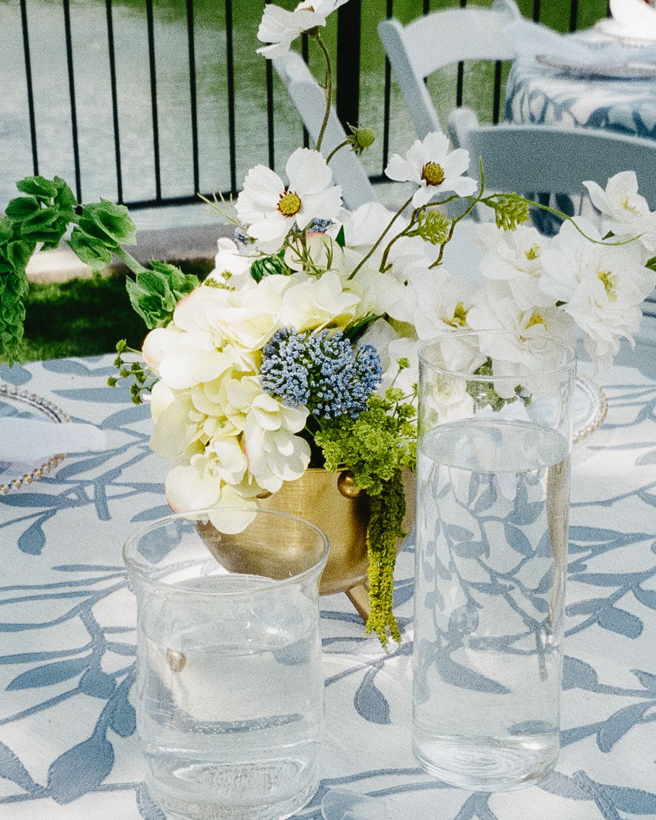 White floral centerpieces in glass vases on a table with blue patterned linens creating an elegant table setting.