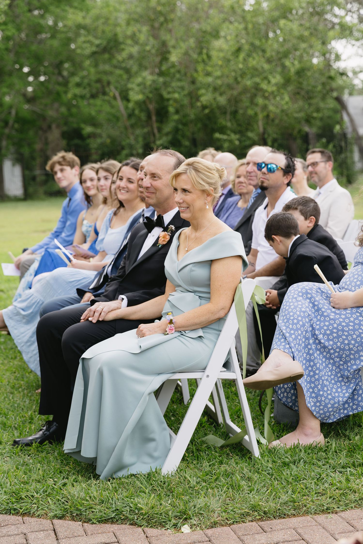 Wedding guests seated on white chairs outdoors for garden ceremony.