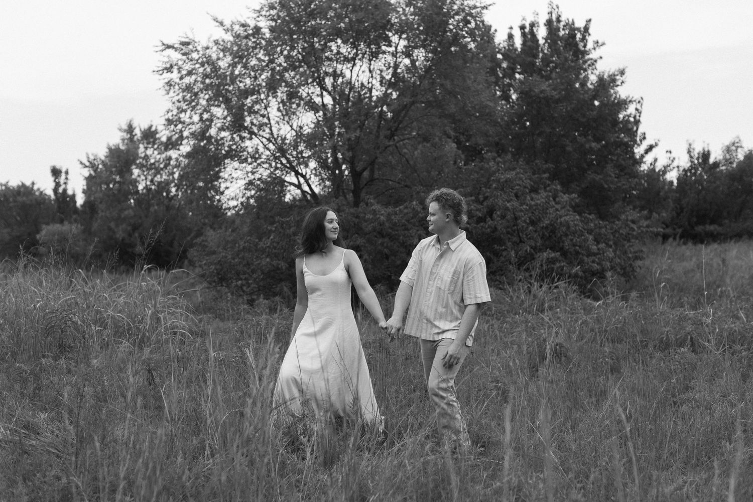 A couple walks together through a rustic meadow in black and white photography.