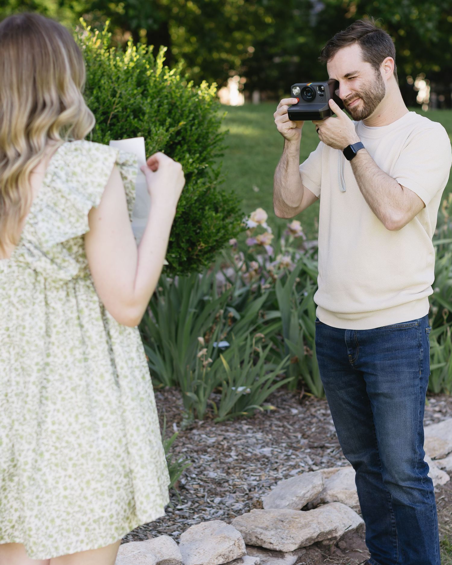 Couple takes photos together in garden setting while holding pregnancy announcement items.