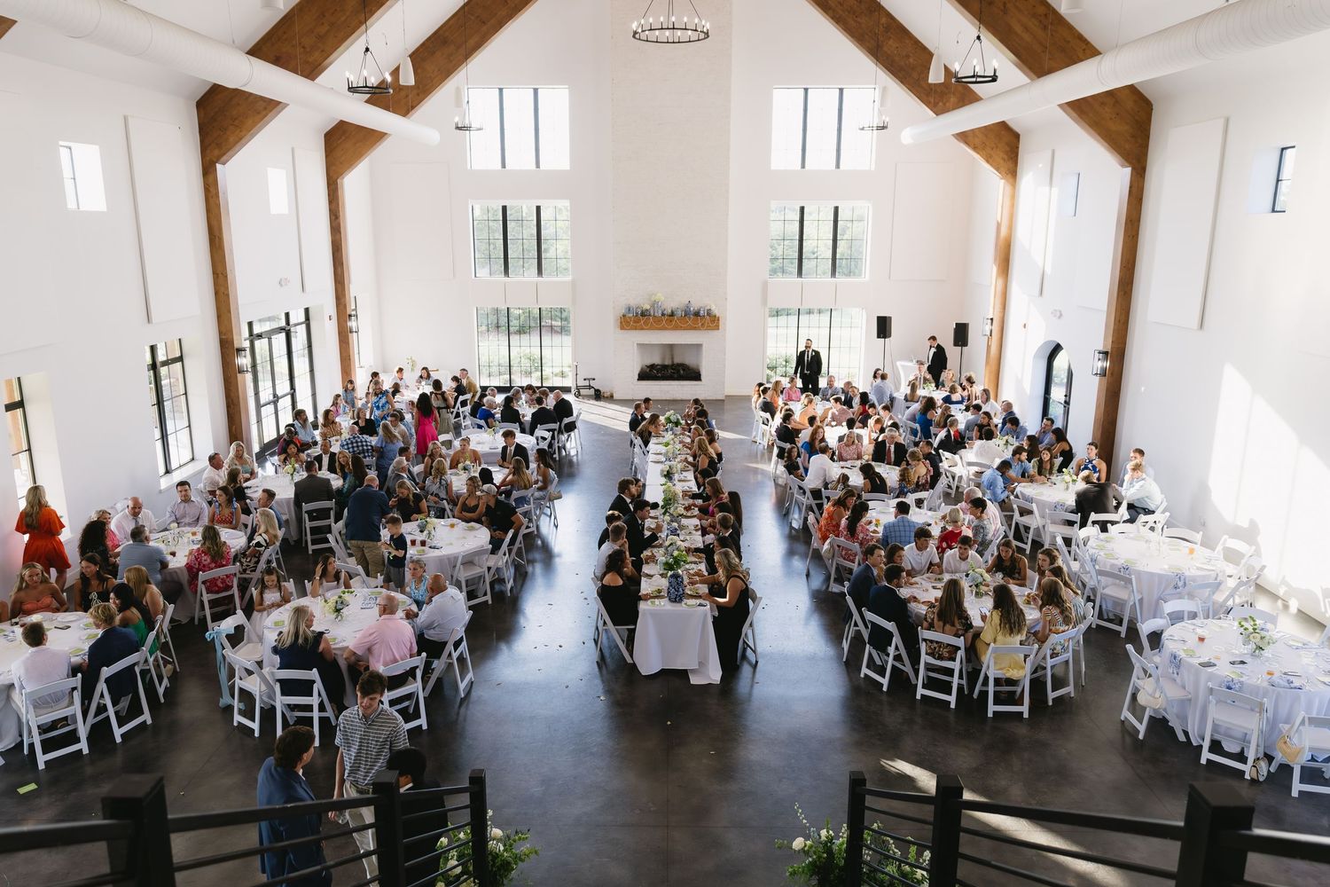 A large wedding reception hall with exposed wooden beams and filled with guests at round tables.