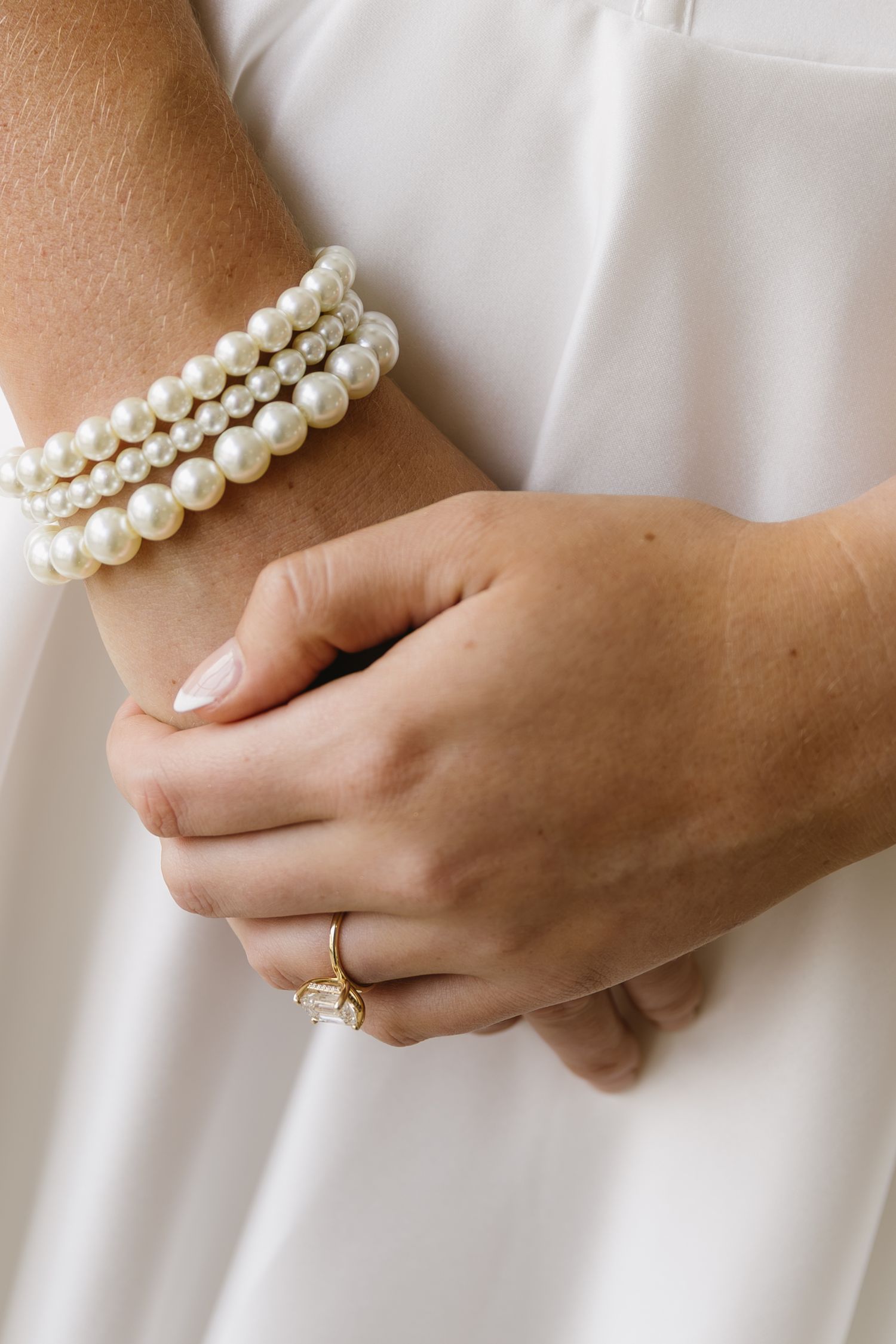 Pearl bracelet and engagement ring detail shot against white fabric.