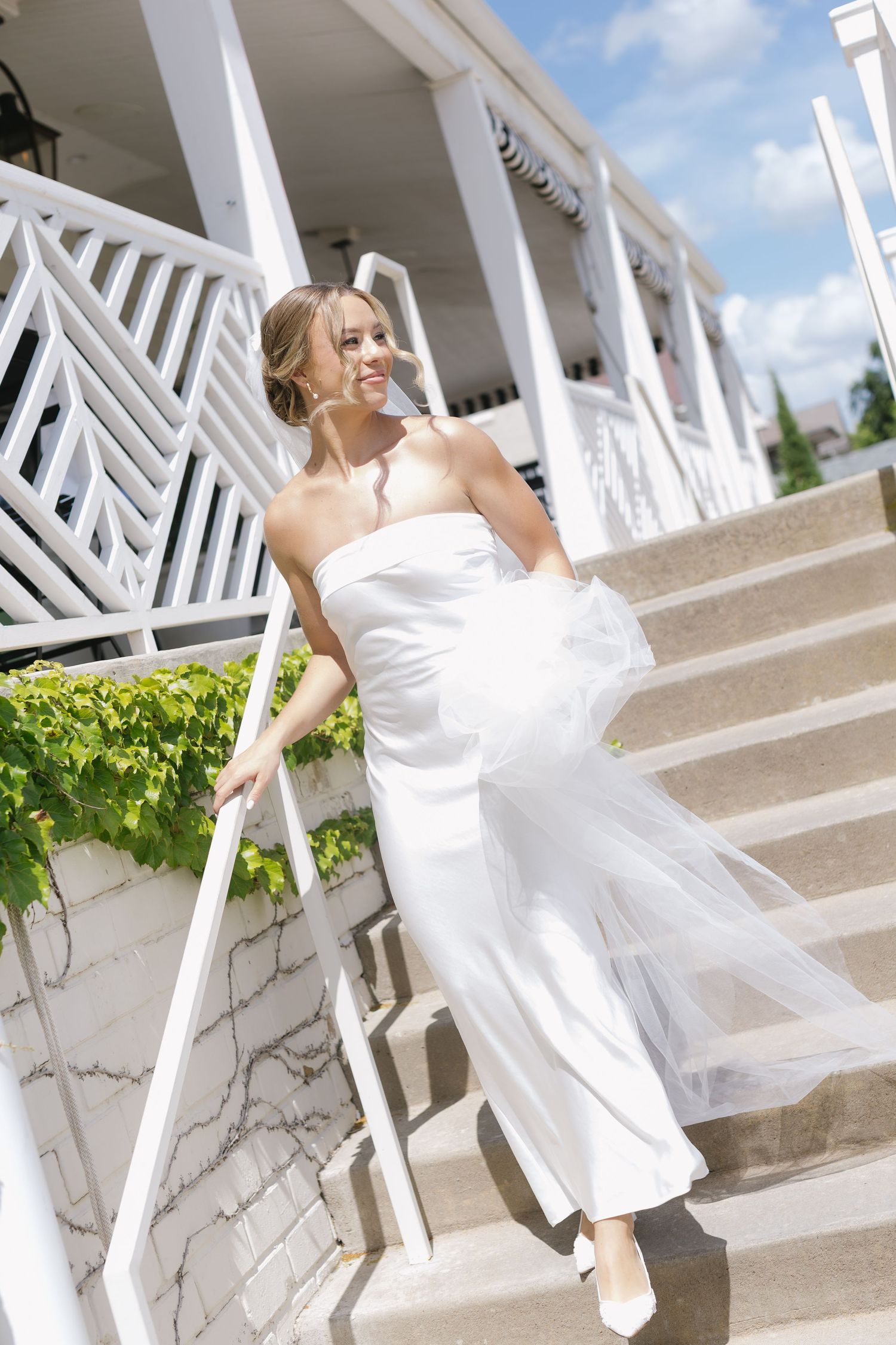 A bride in a flowing white dress twirls playfully on white marble stairs outdoors.
