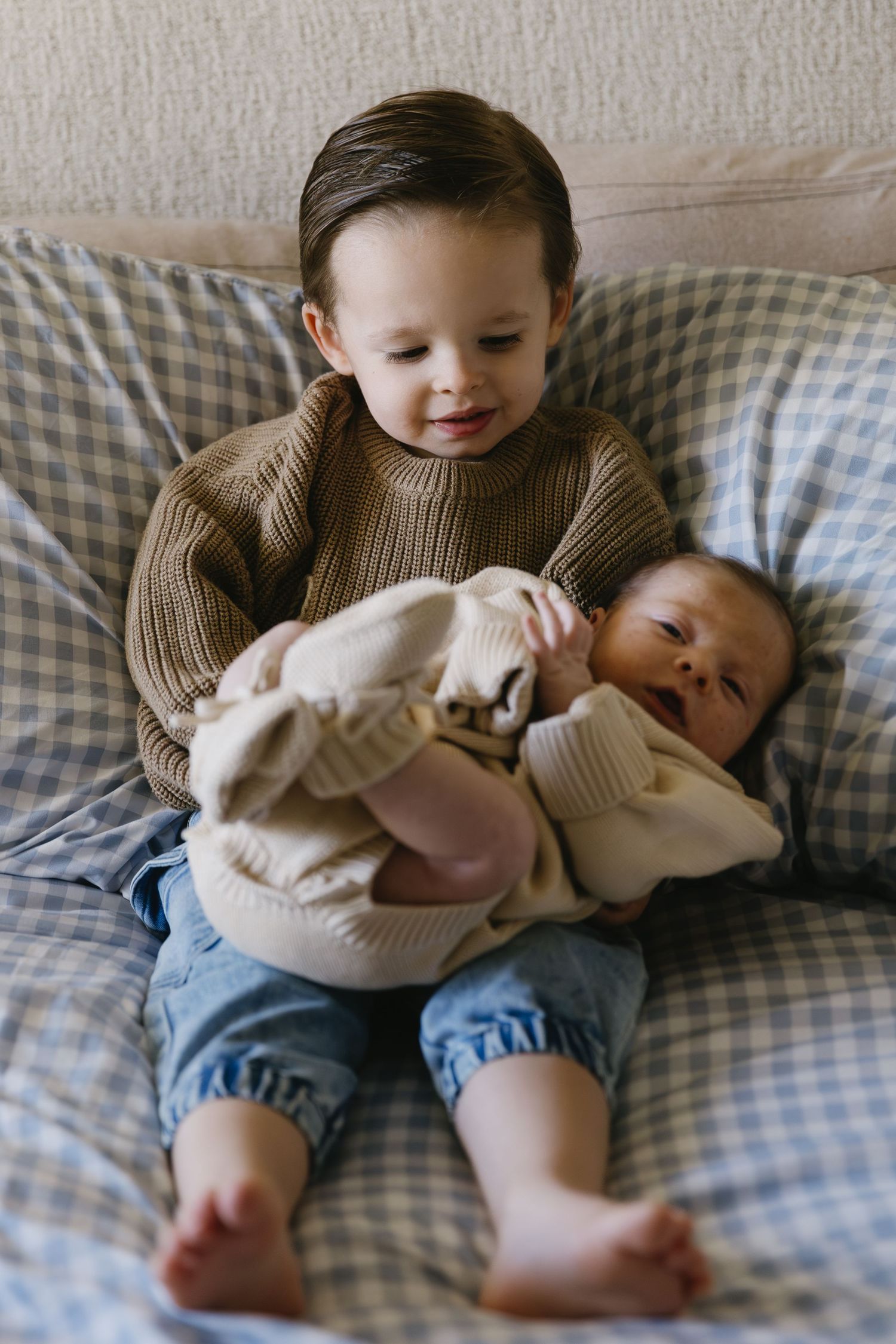 Two siblings in matching sweaters sharing tender moments on checkered bedding.