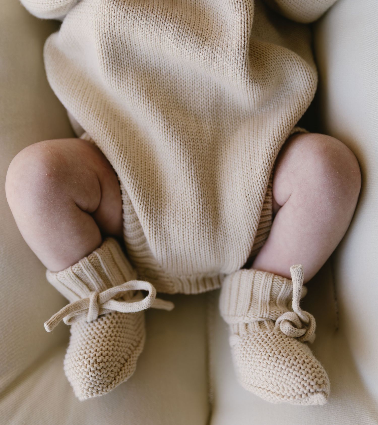 Close-up of tiny feet wearing cream knitted booties with bow details.