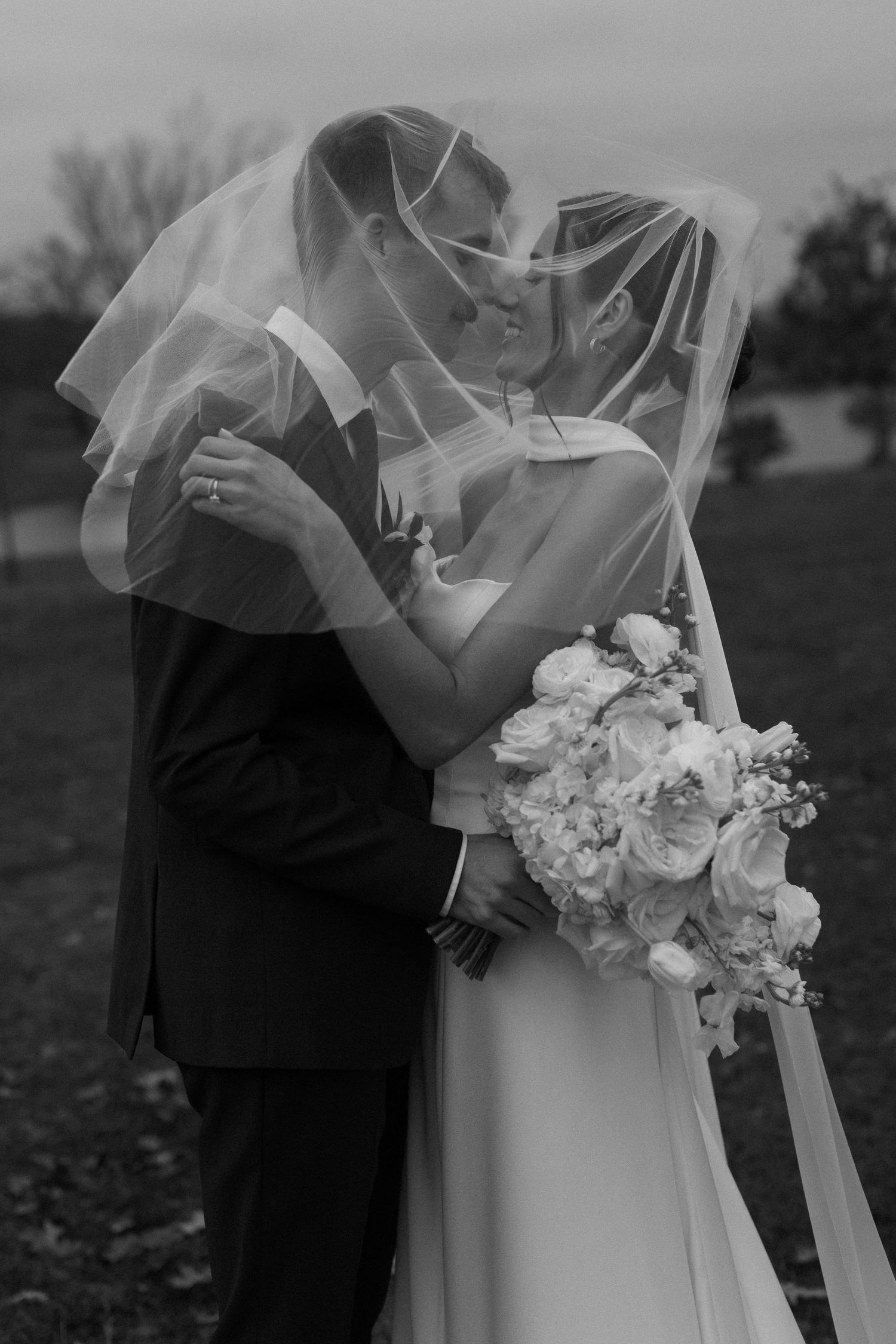 Intimate black and white wedding moment captured with bride's veil flowing in the breeze.