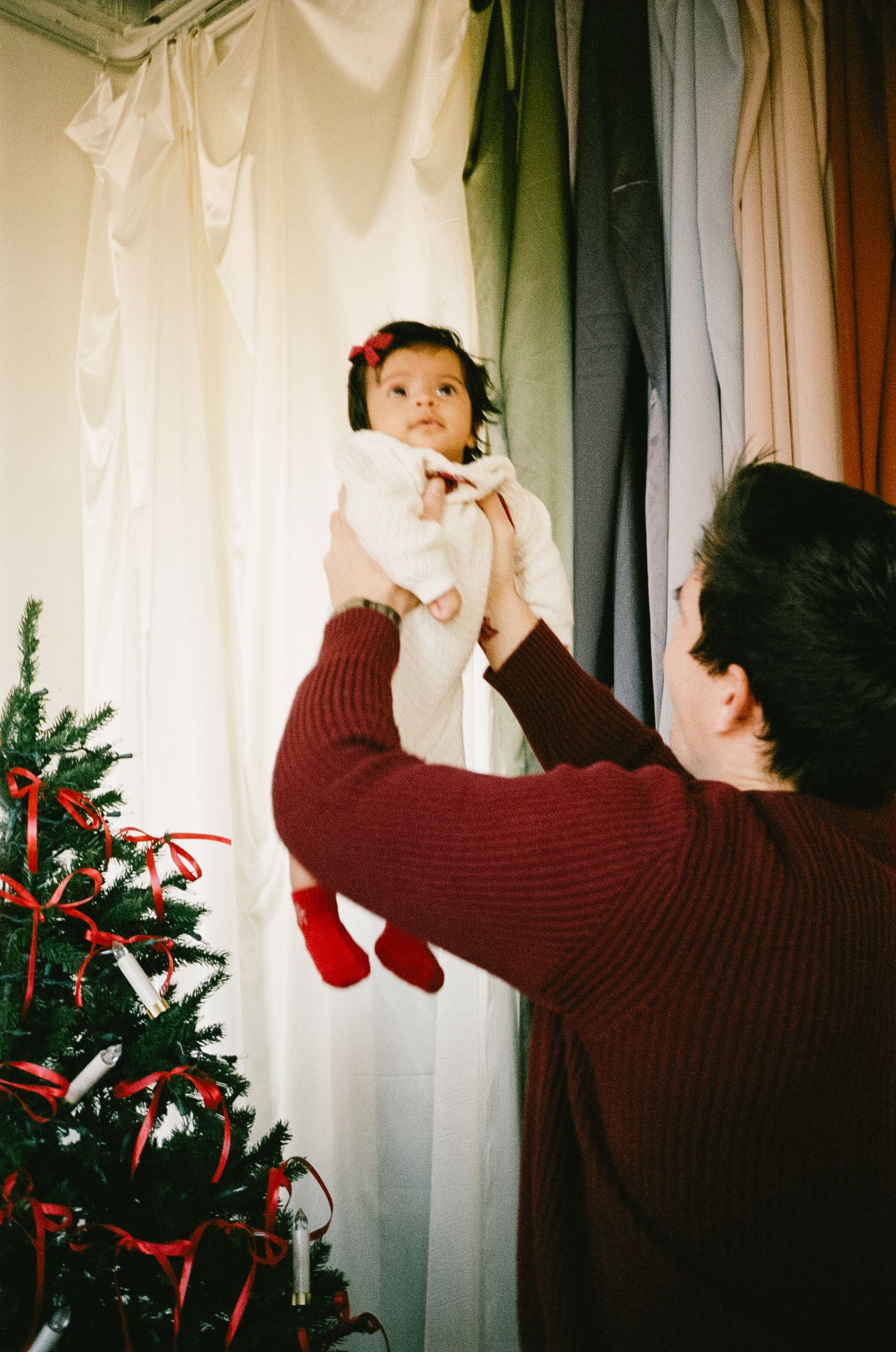 Four sequential photos show someone hanging white curtains on a window with a small Christmas tree visible in the frame.