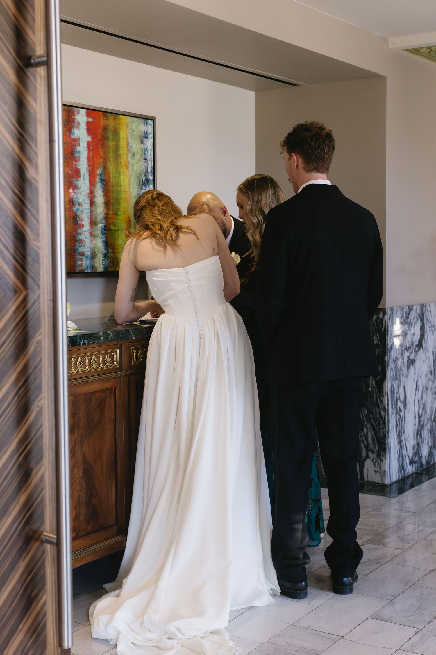 A wedding couple and guests gather in front of a colorful abstract painting in an elegant hallway.