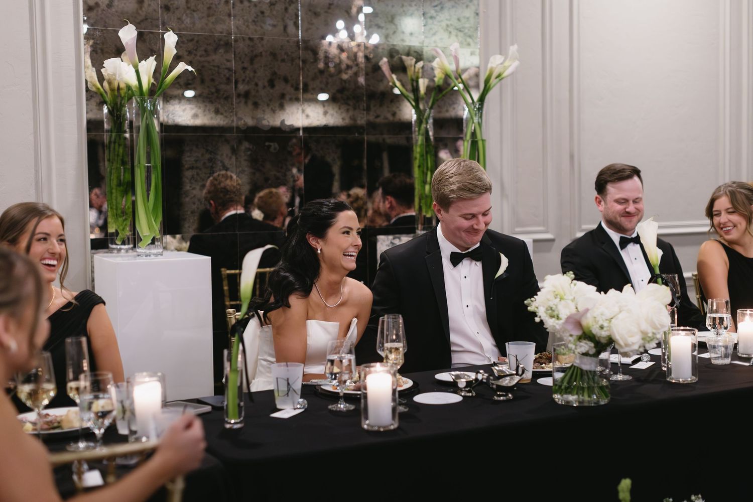 Wedding reception dinner scene with elegant white floral centerpieces and black tablecloths.