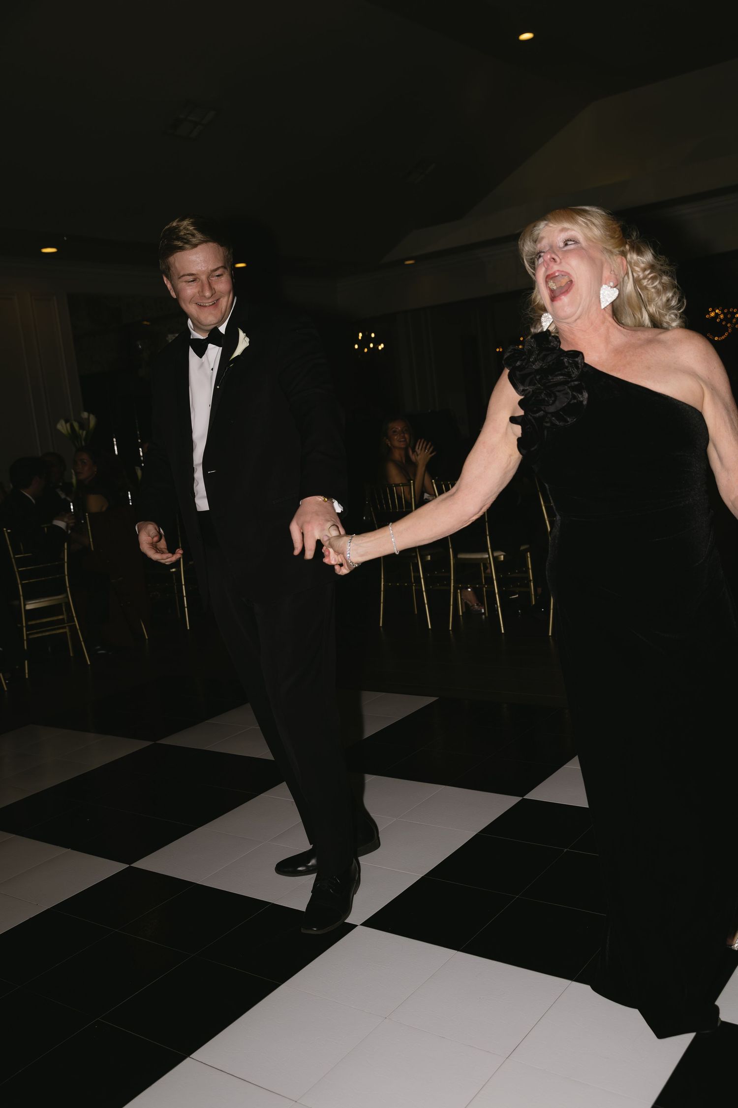 Couples dance on a black and white checkered dance floor at an evening wedding reception.