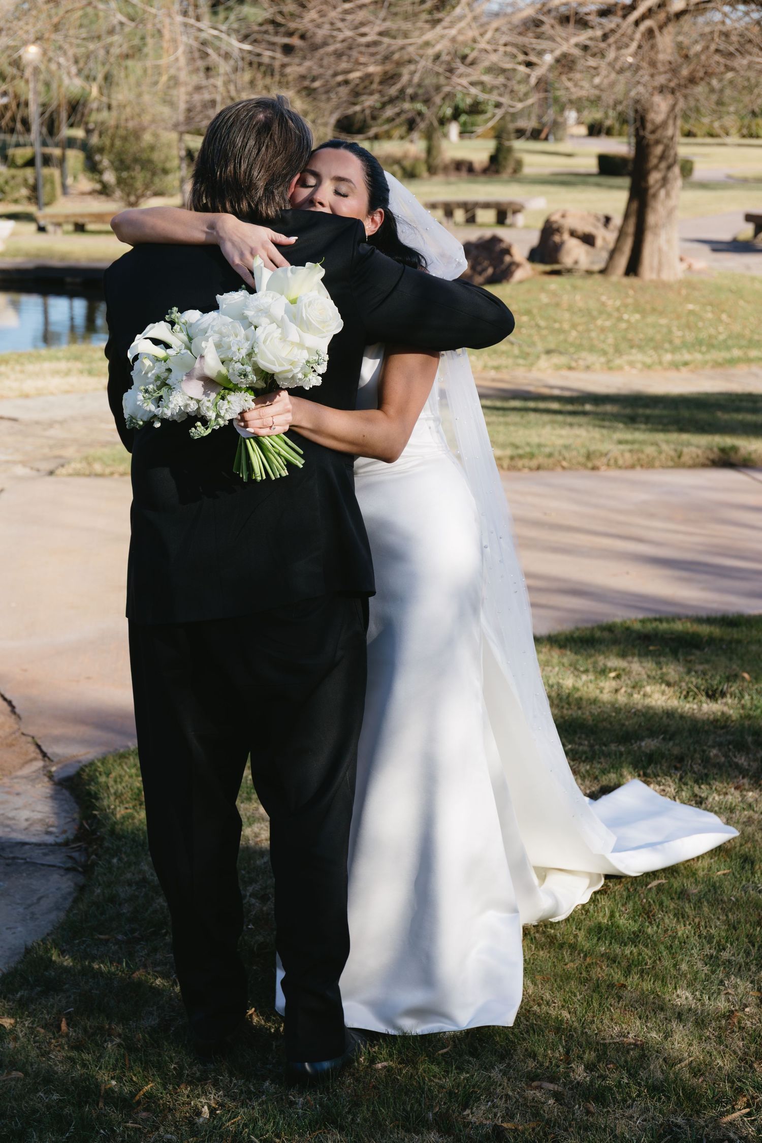 Emotional embrace between newlyweds with white floral bouquet outdoors.