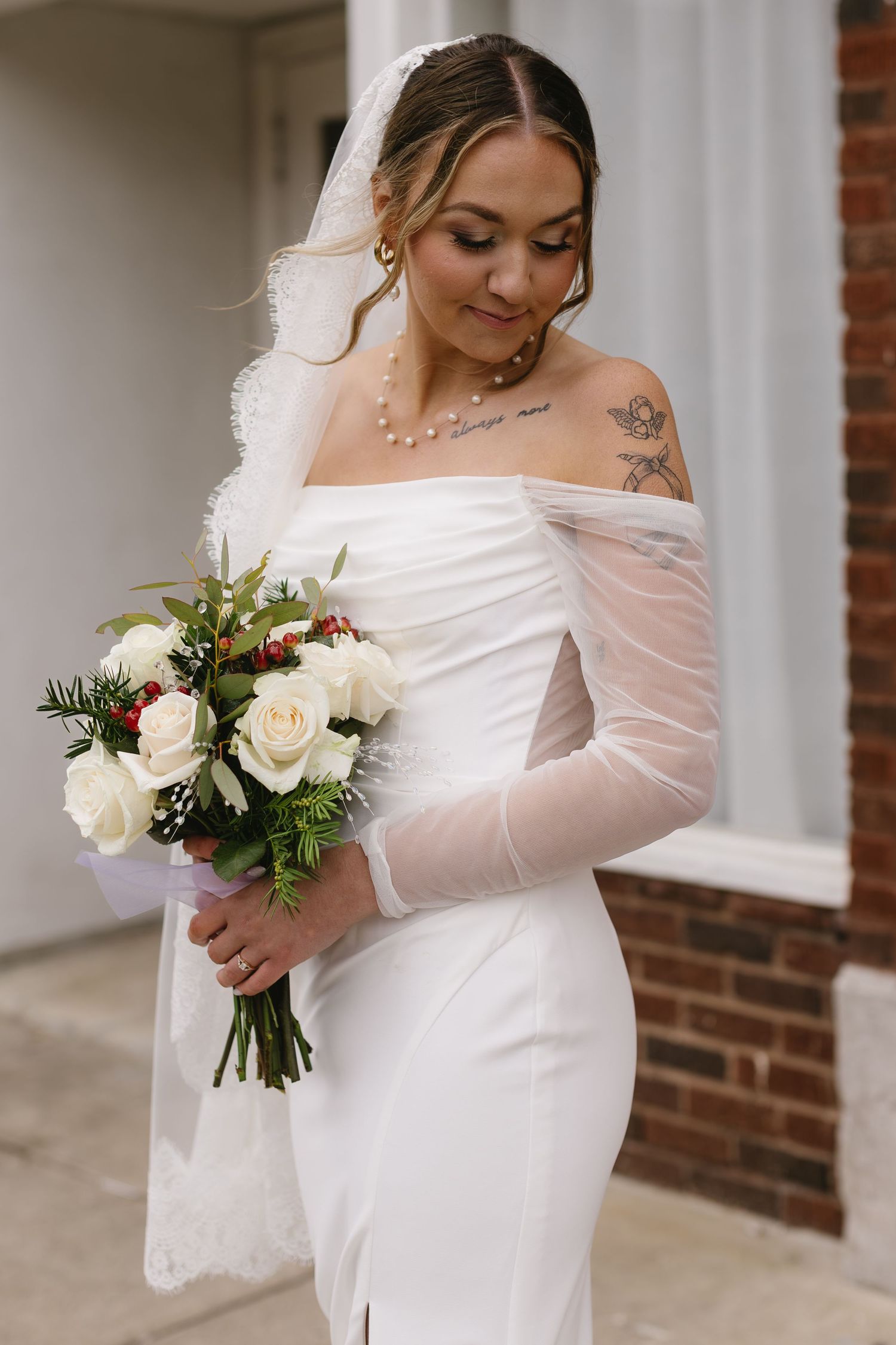 Bride in off-shoulder wedding dress holding a white and green floral bouquet.