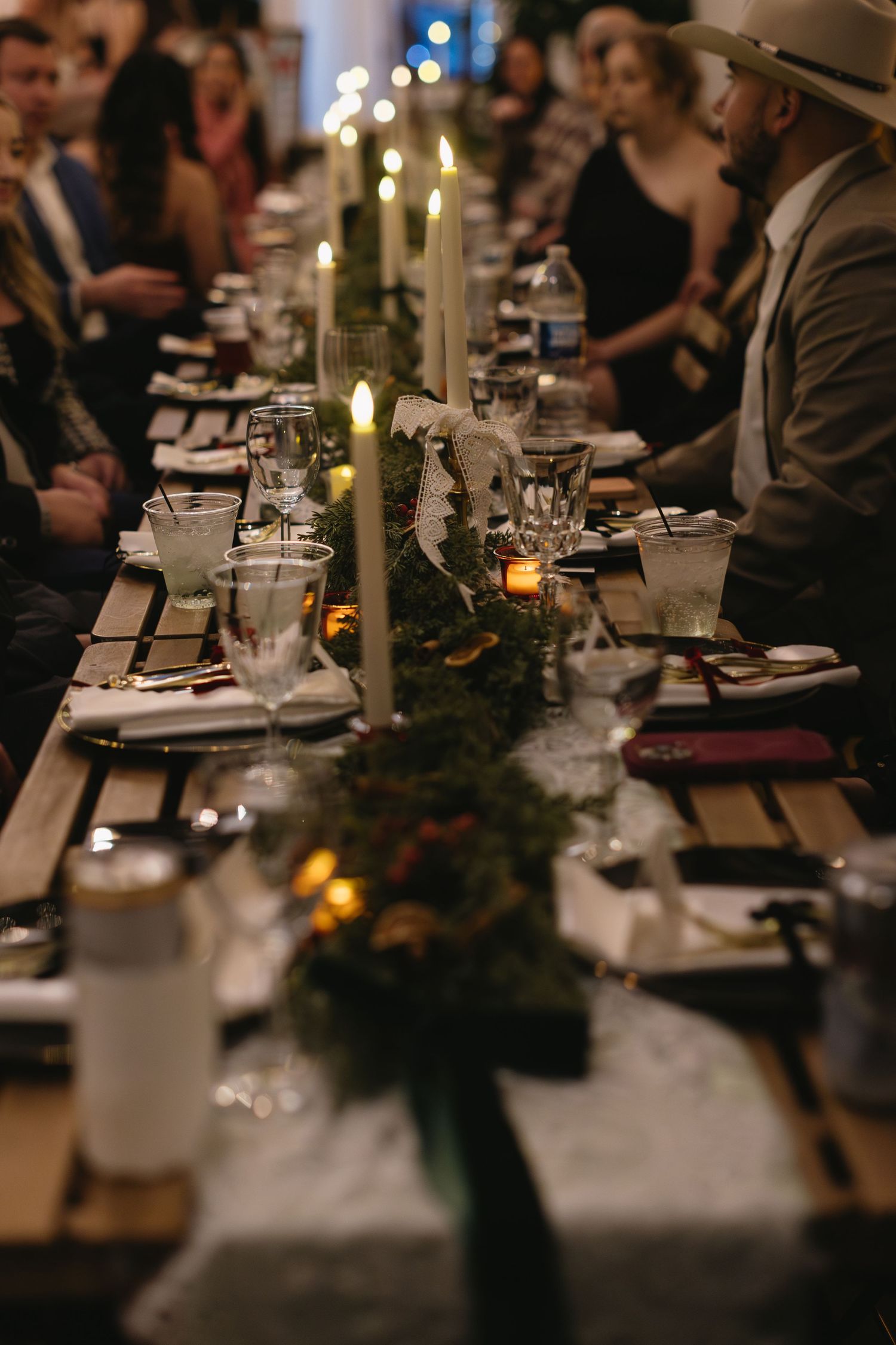 Elegant candlelit wedding reception table with place settings and greenery decorations.