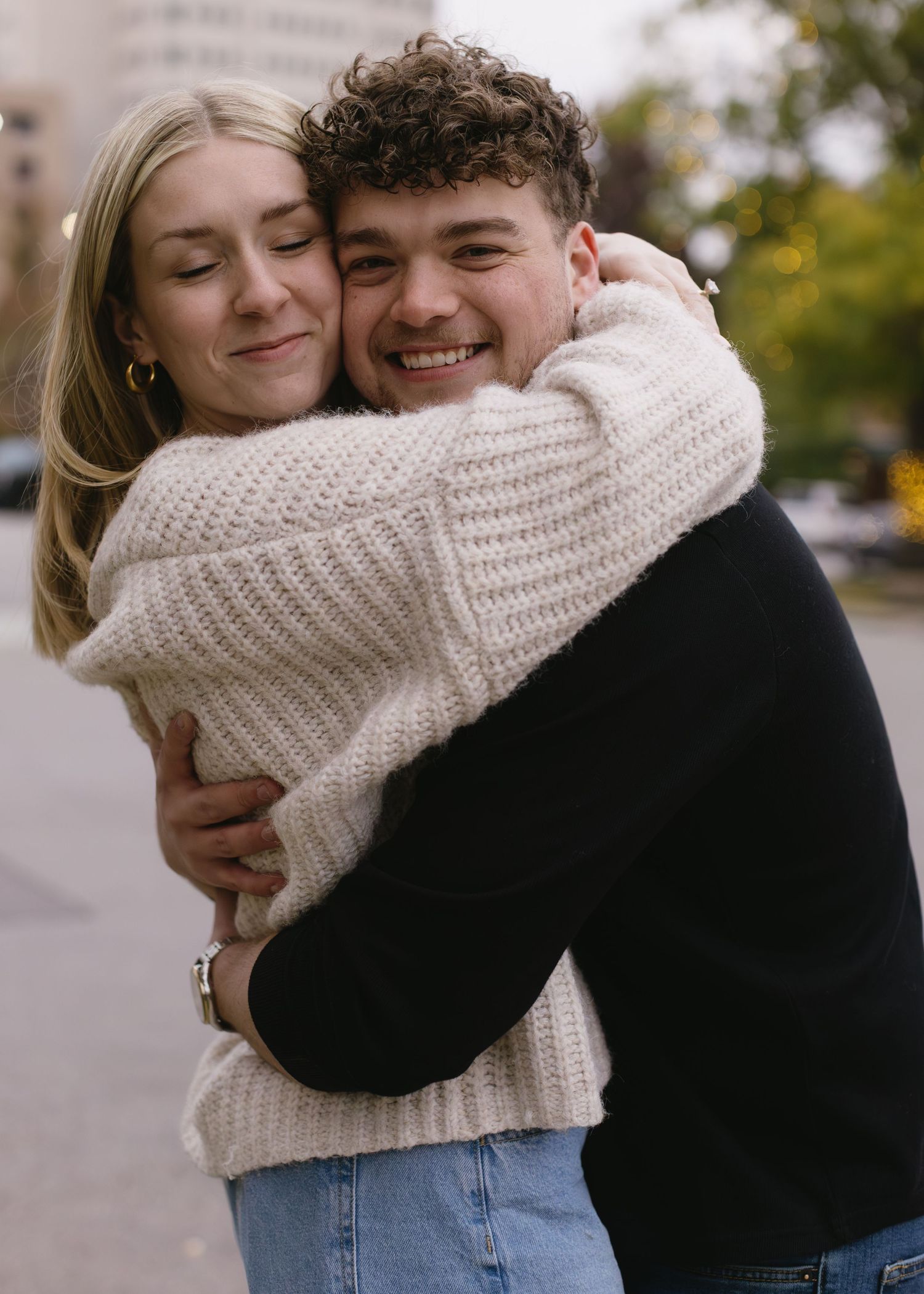 A couple embraces warmly outdoors wearing coordinated casual fall outfits.