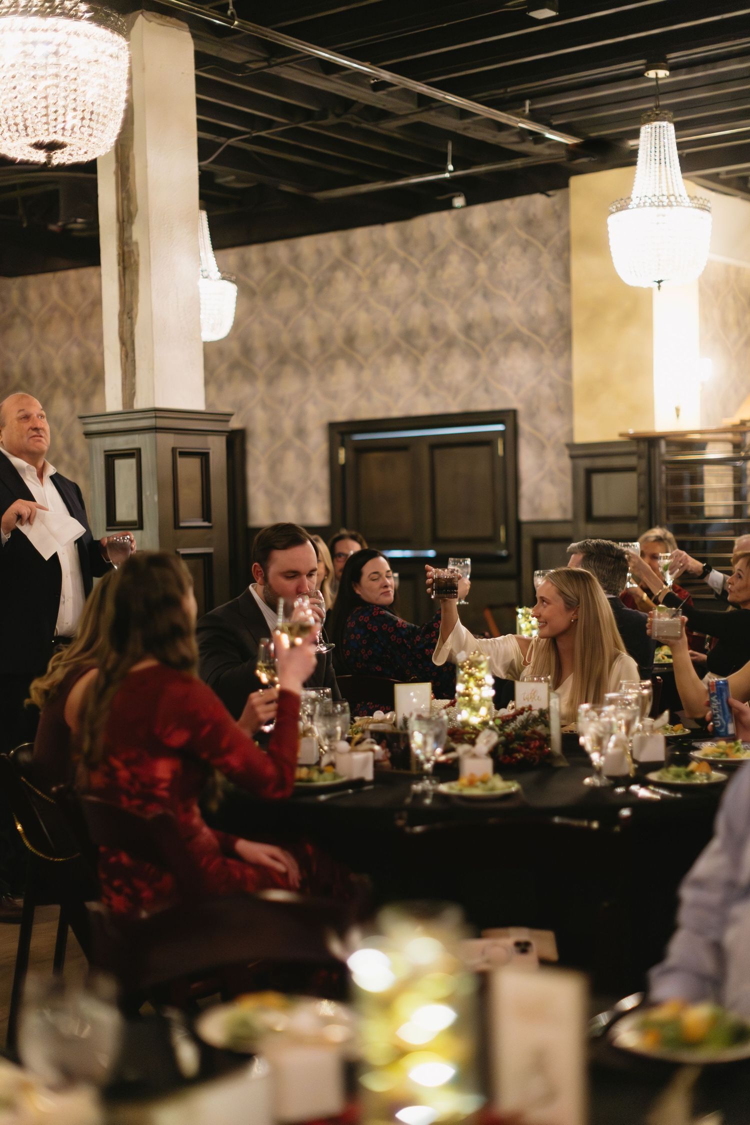 Elegant dining room with crystal chandeliers and guests seated at tables during an evening event.