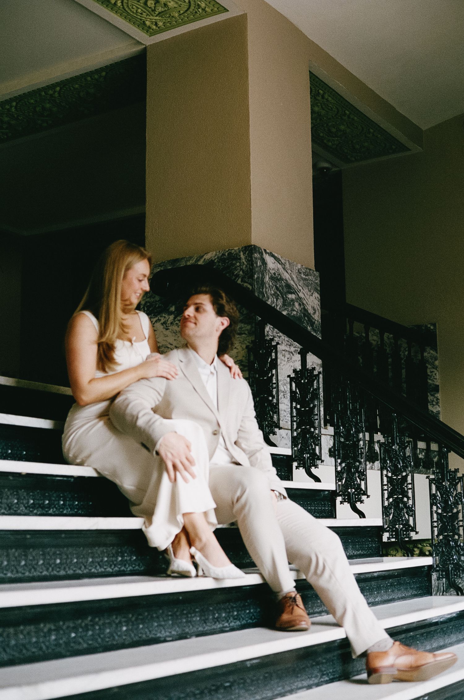 A couple in formal attire shares a quiet moment on ornate stone steps.