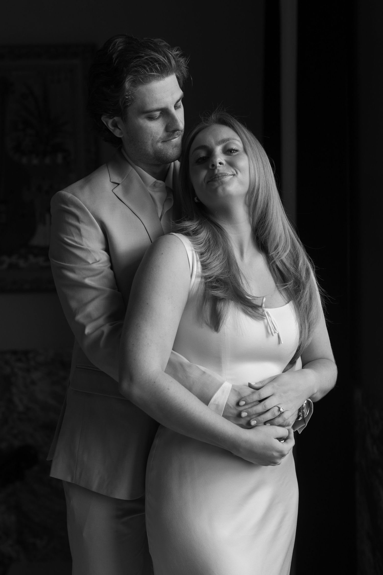 An intimate black and white portrait of a couple in formal wear sharing a tender moment.