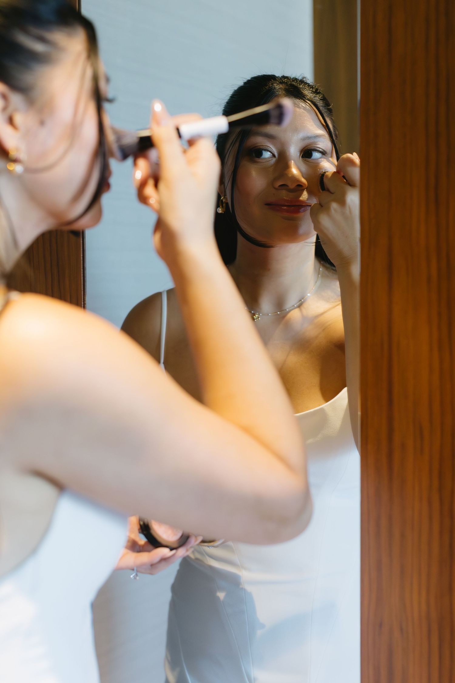 Wedding preparation scene showing makeup application in a softly lit room.