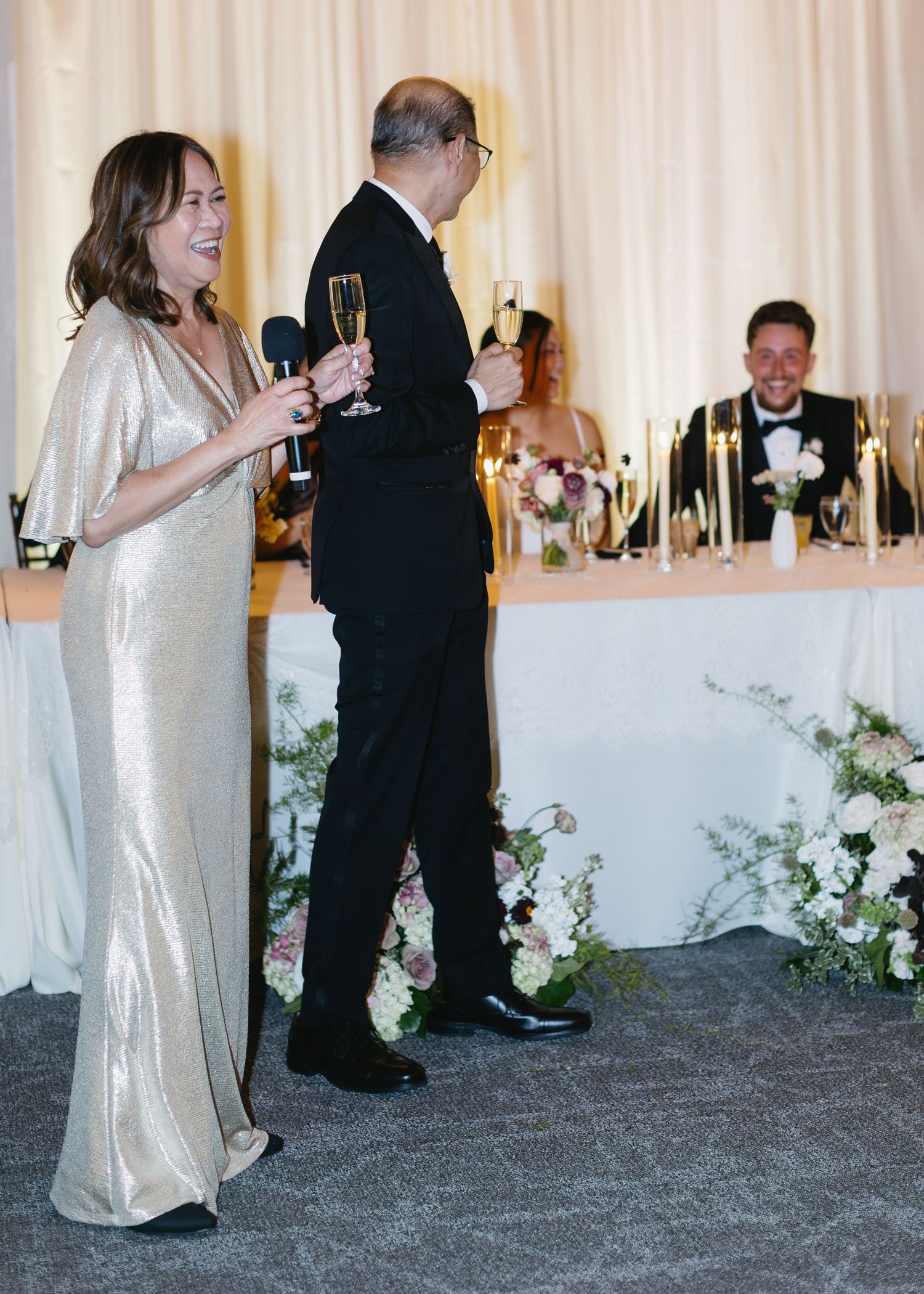 Wedding guests mingling and dancing by a decorated head table with white floral arrangements.