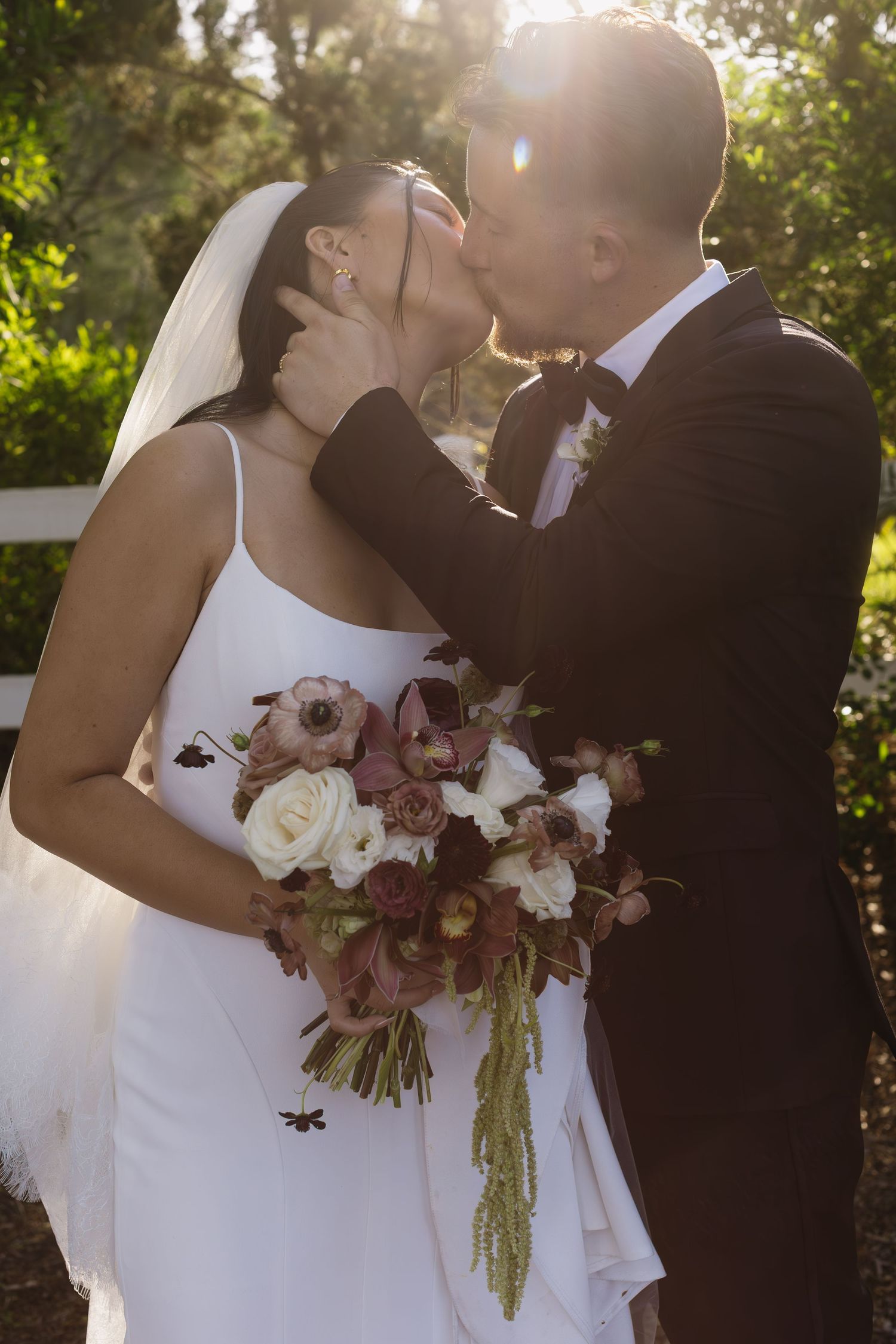 A romantic wedding moment captured at sunset with a floral bouquet in burgundy and white.
