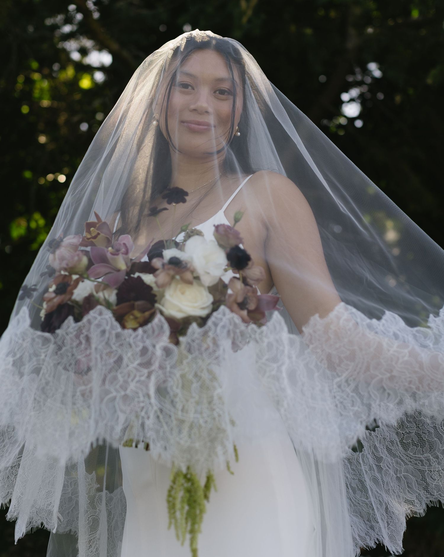 A bride wearing a delicate lace veil poses outdoors in a series of romantic bridal portraits.