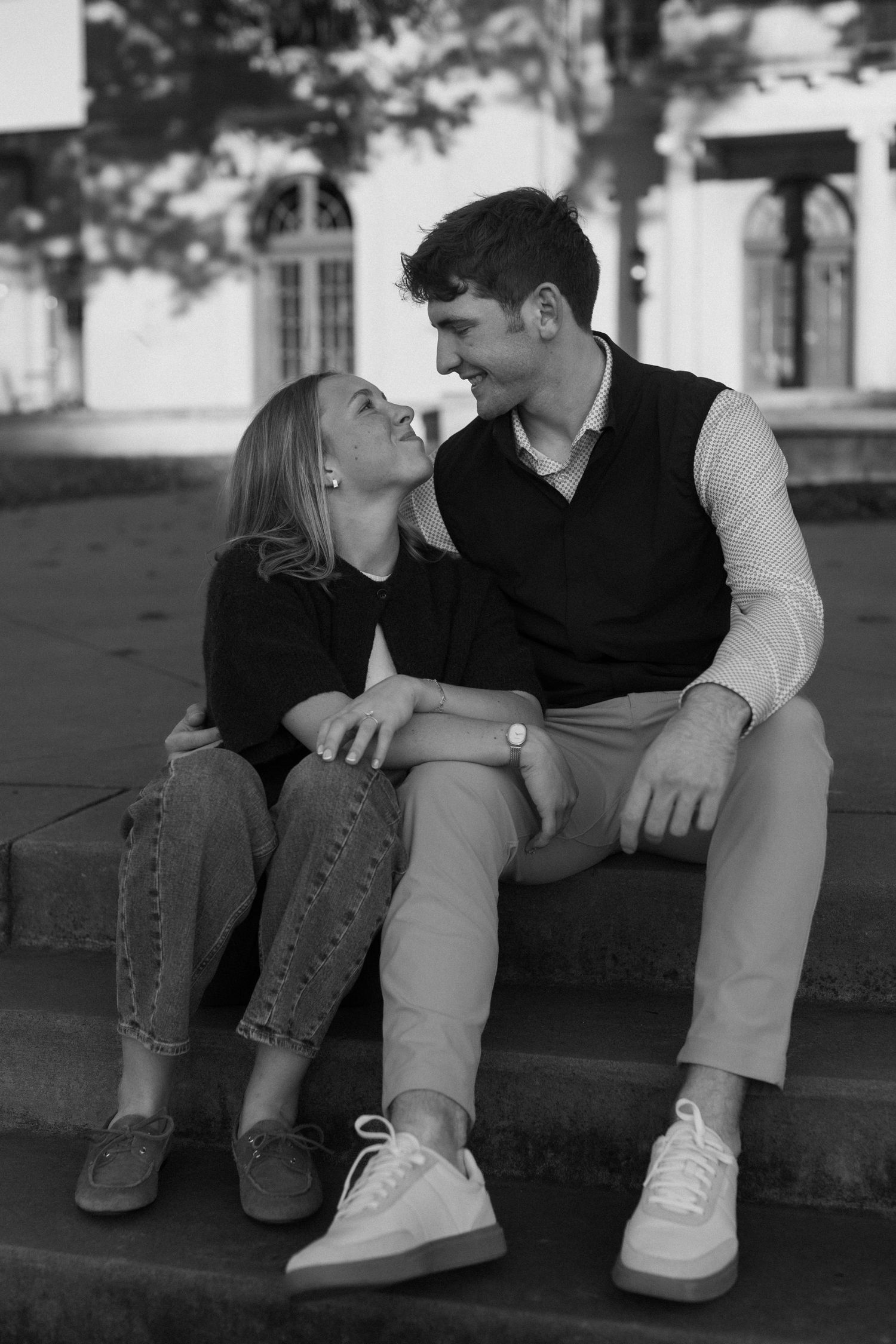 Black and white photo of a couple sitting close together on steps wearing casual attire.