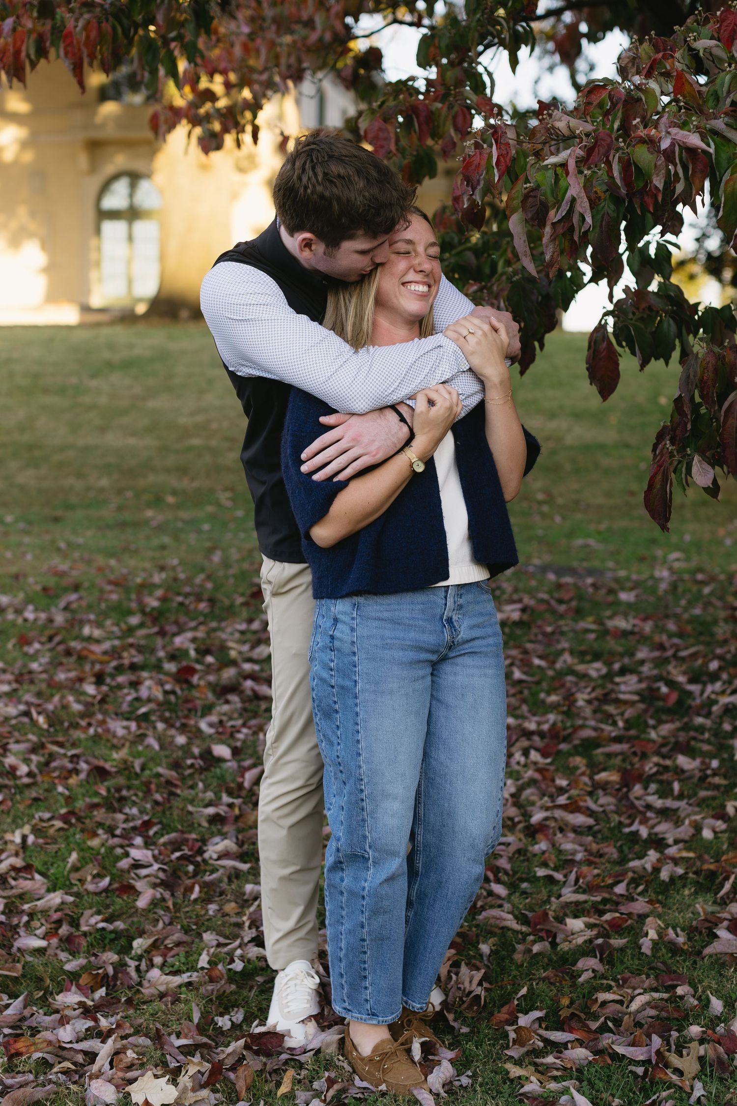 A tender moment shared between a couple under autumn trees with falling leaves.