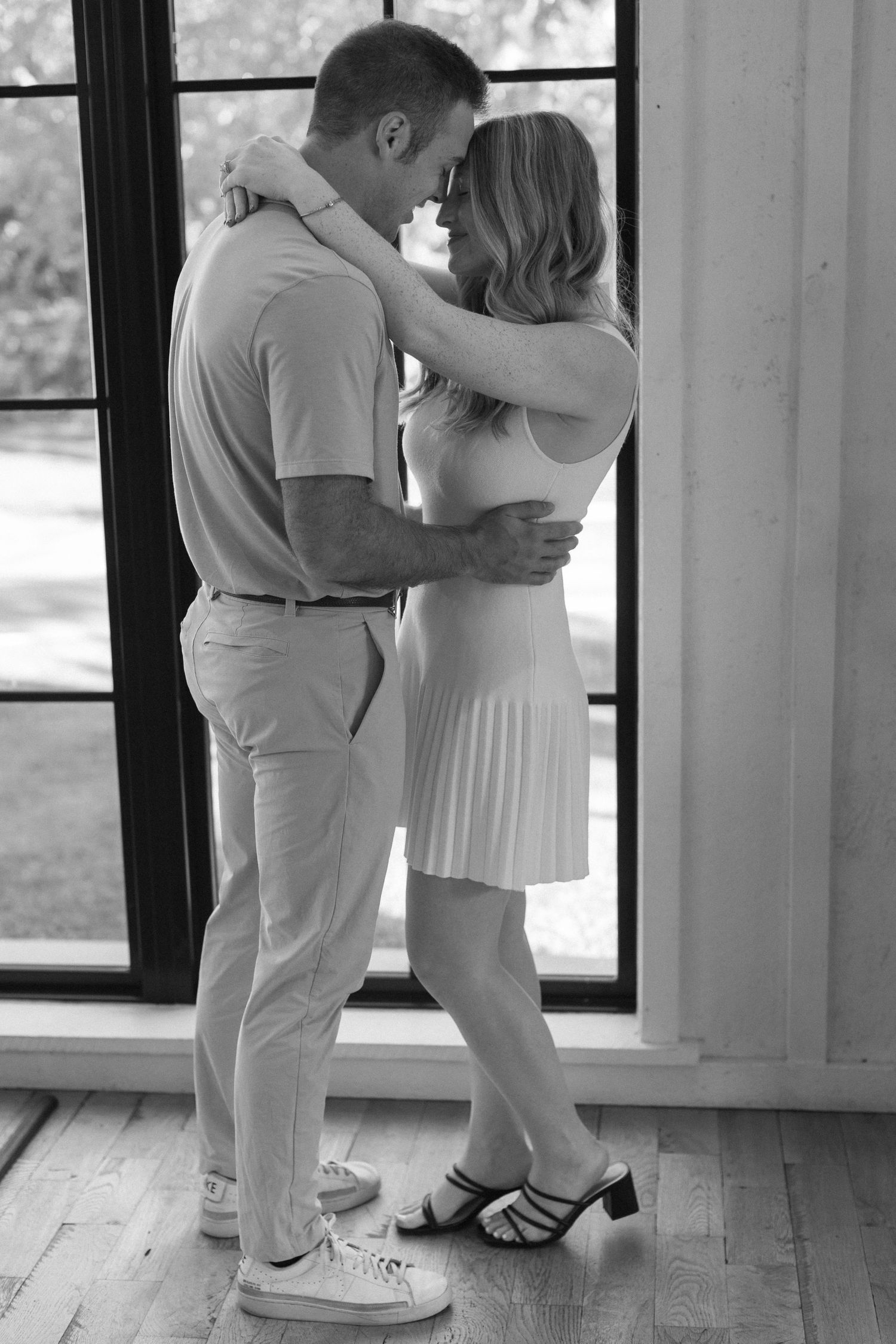 Black and white photos of a couple dancing together on a wooden floor near large windows.