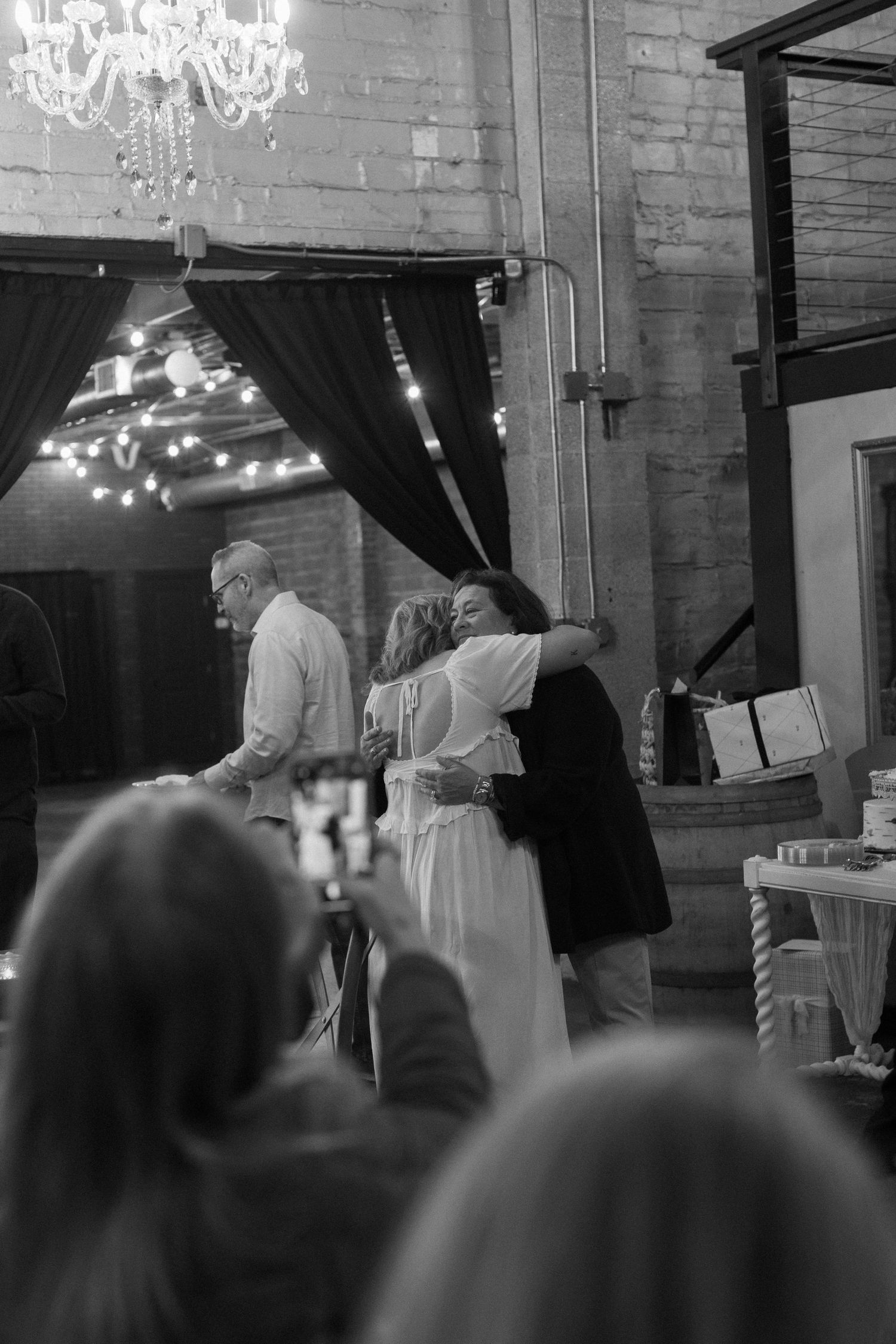 Black and white photo of celebration moment at wedding reception with chandelier overhead.
