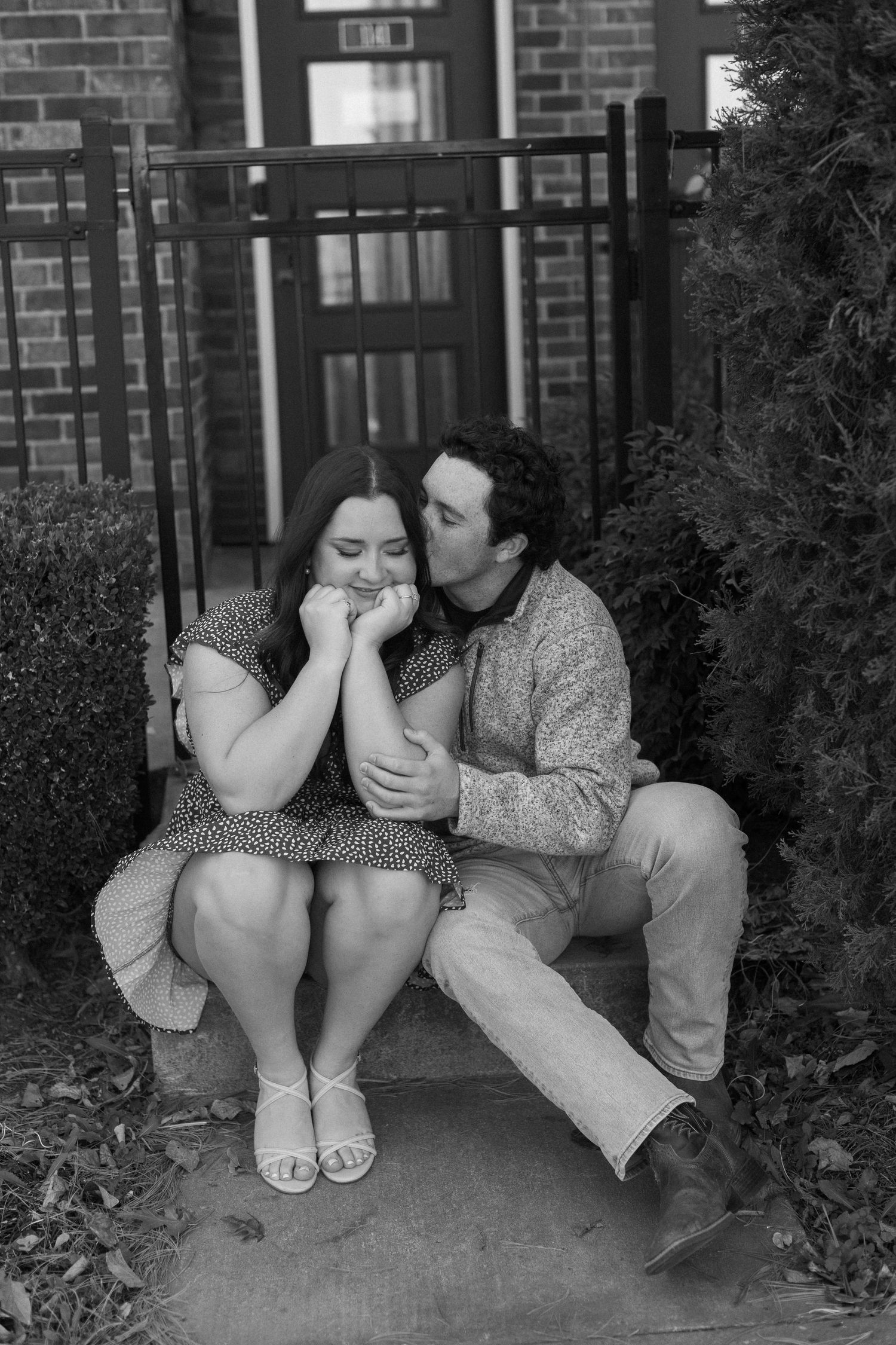 A couple sits close together on brick steps during an intimate black and white photoshoot.